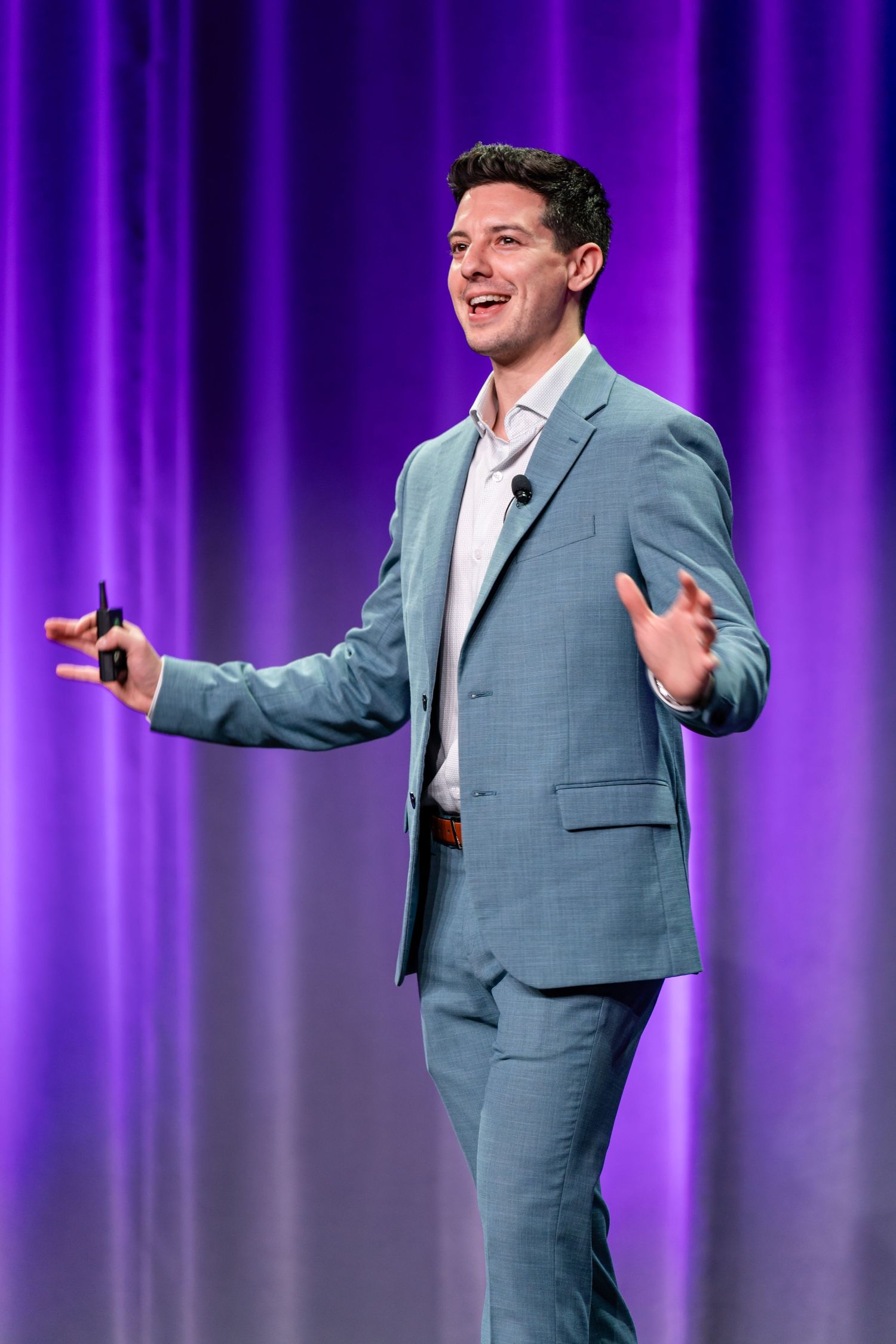 Dynamic speaker gestures while presenting on stage with purple curtain background.