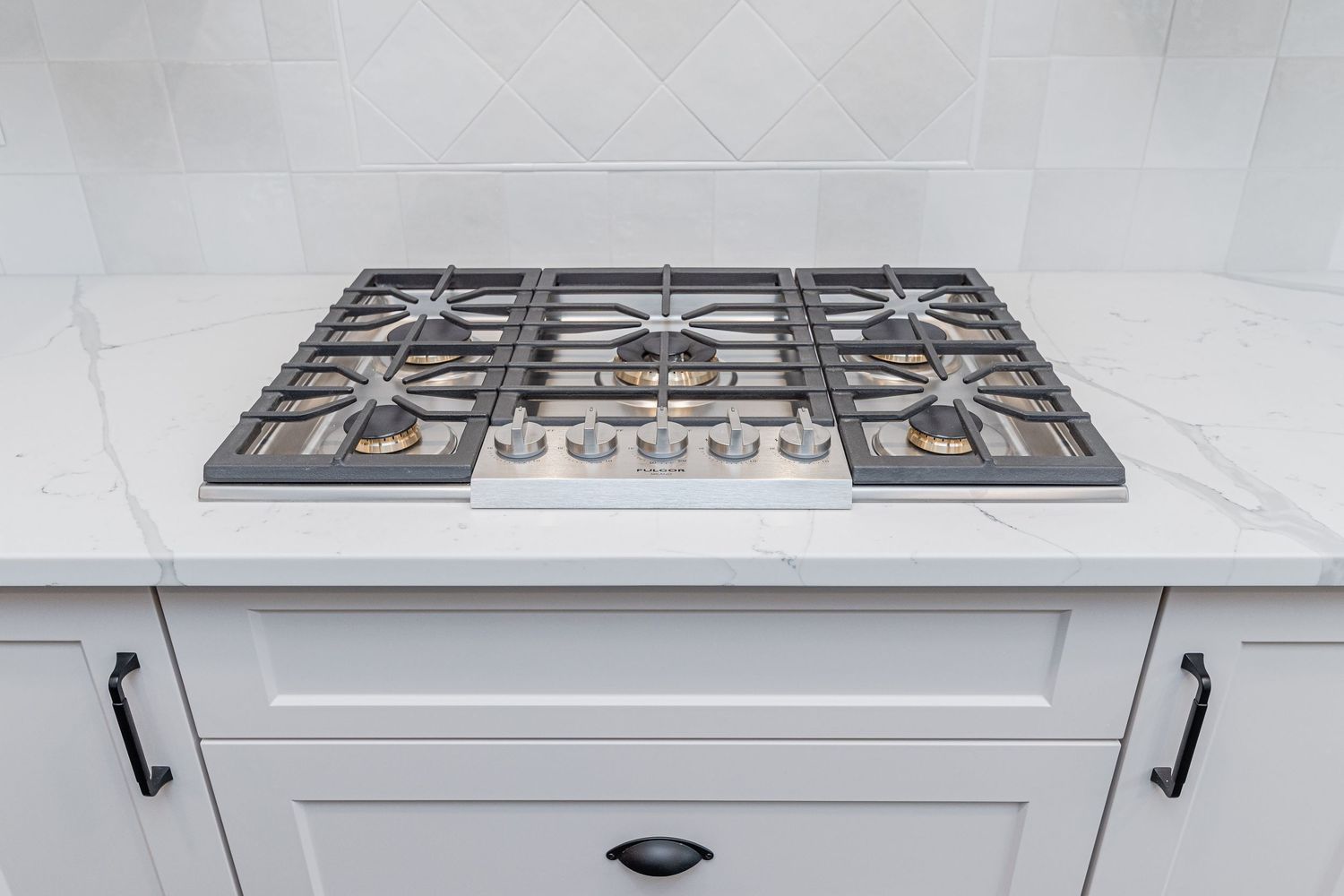 Stainless steel 5-burner gas cooktop installed in white shaker cabinet kitchen island with marble countertop.