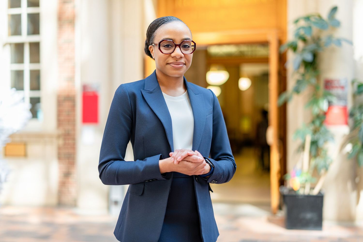 Professional in a navy blazer standing in front of an office building with brick walls.