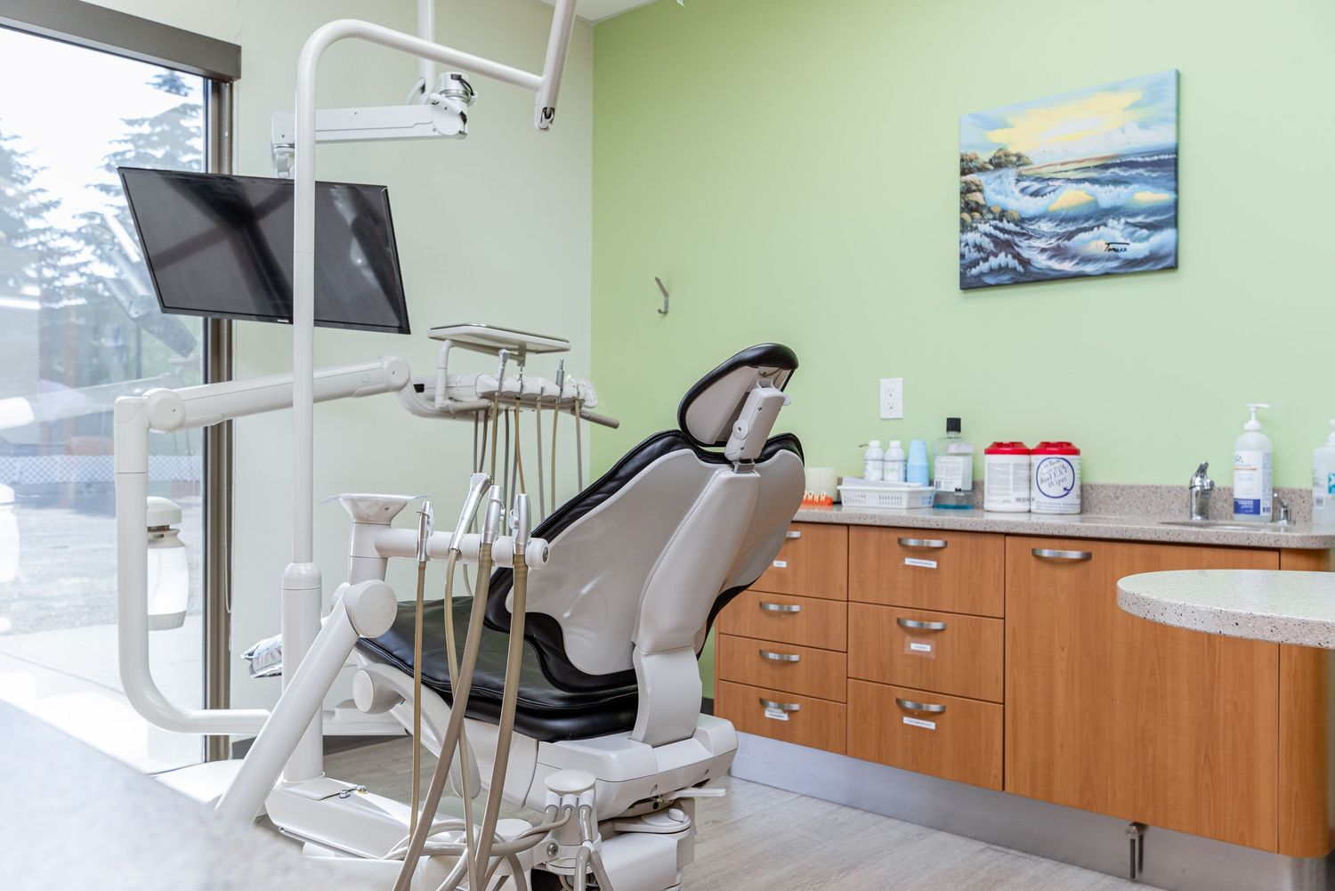 Clean and modern dental treatment room with green walls and wooden cabinets.