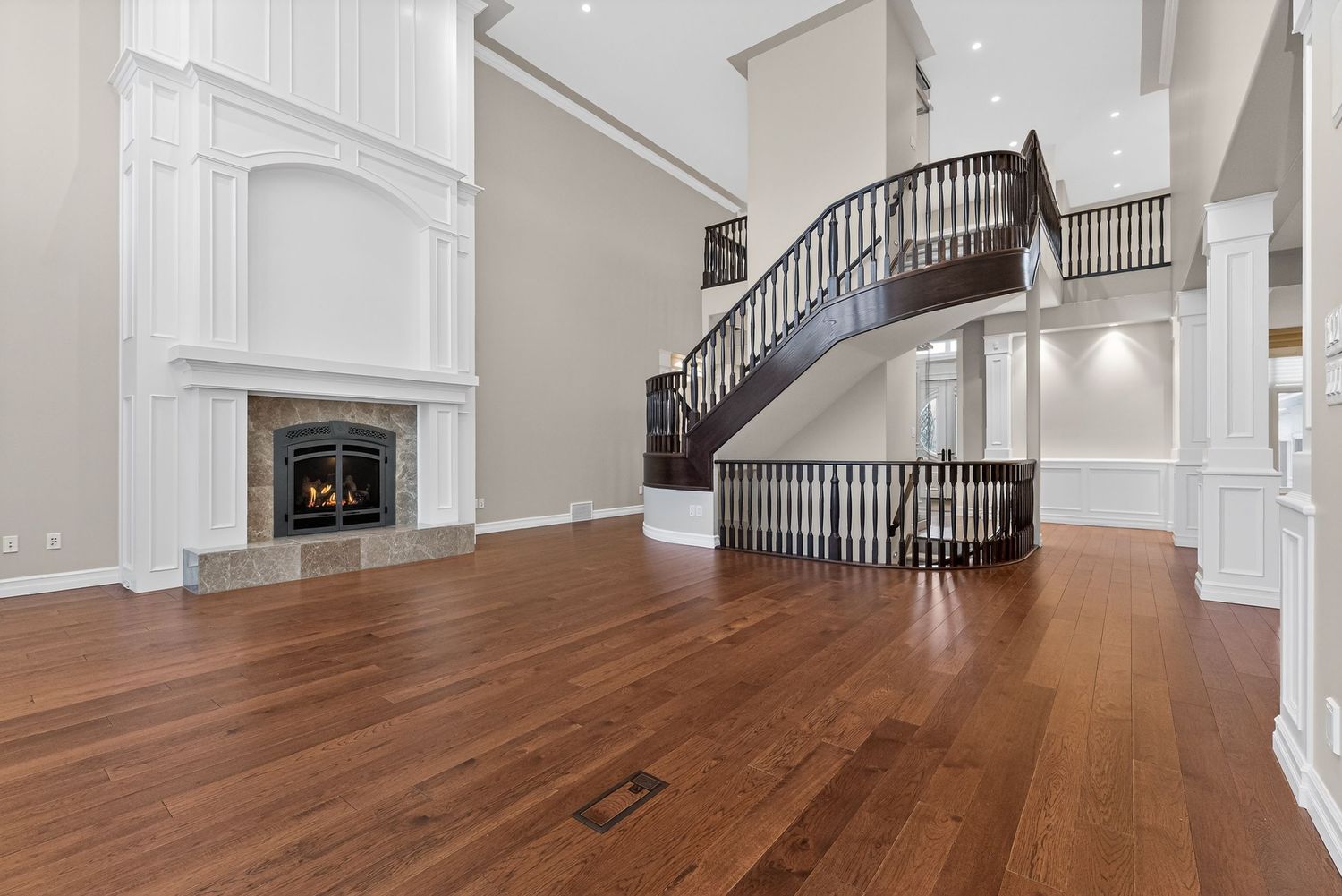 Elegant two-story living room with hardwood floors, white fireplace, and curved dark wood staircase.