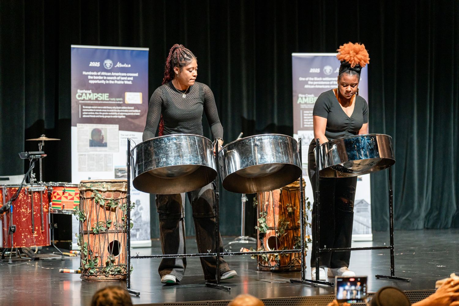 Performers playing drums on stage during a cultural performance with dramatic lighting.