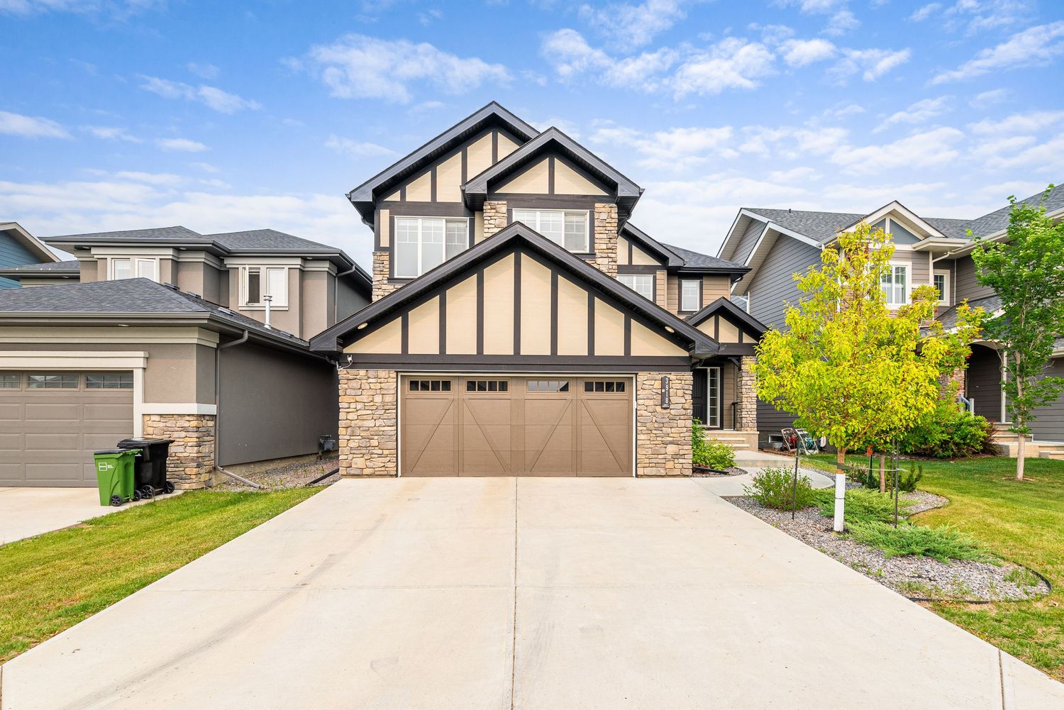 Tudor-style two-story home with stone facade, double garage, and manicured lawn under blue skies.