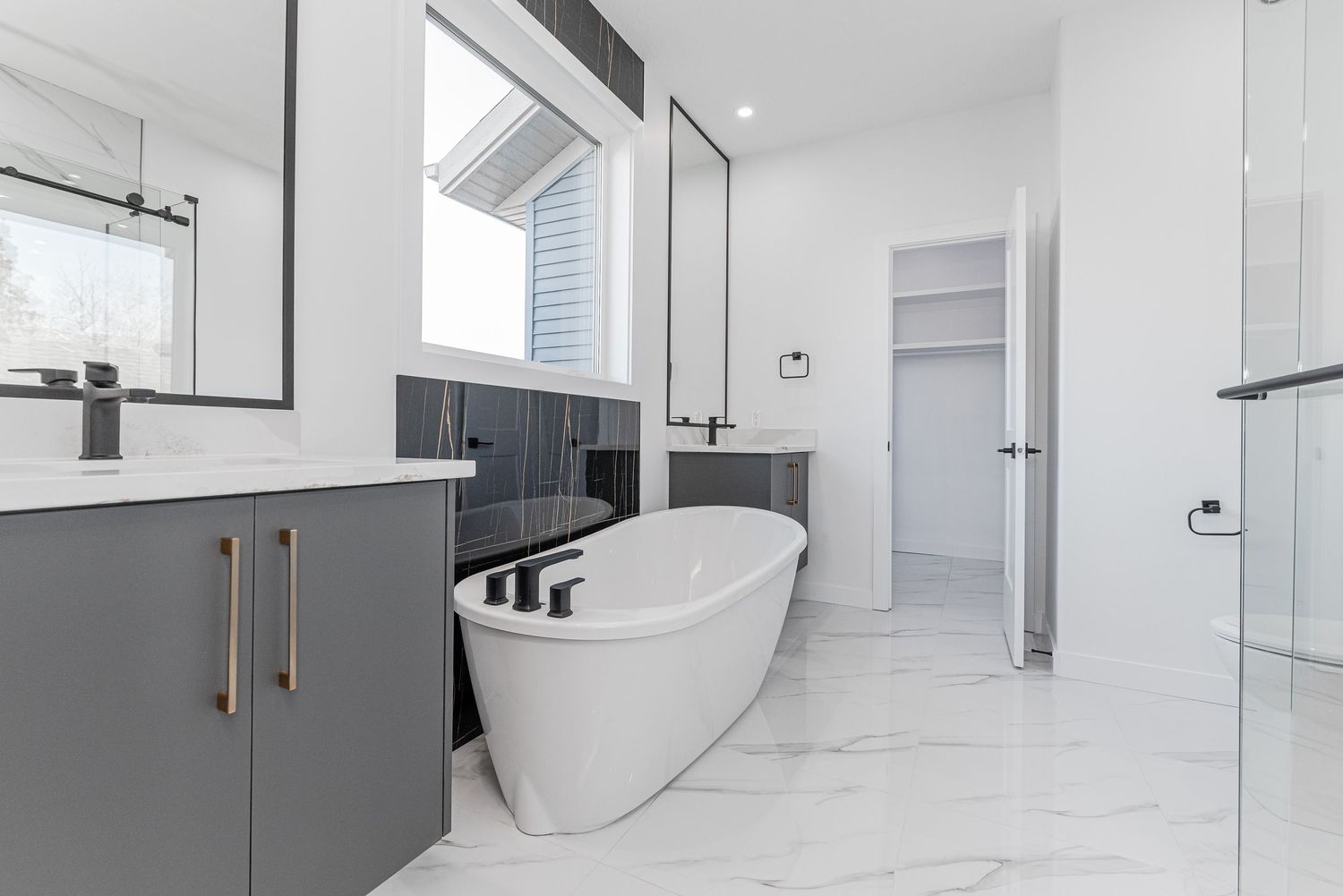Modern bathroom with freestanding soaker tub, gray vanity, marble floors, and glass shower enclosure.