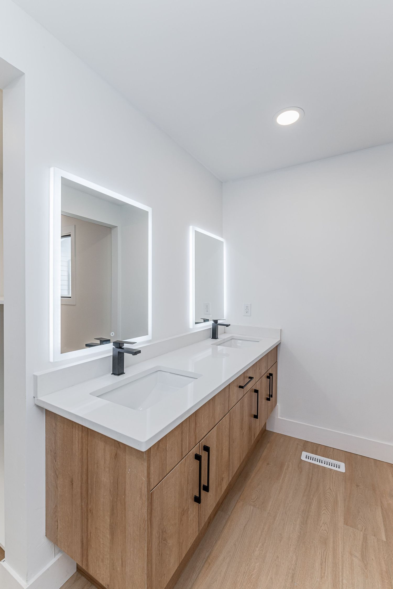 Modern double vanity bathroom with LED mirrors, wood cabinets, black fixtures, and white quartz countertops on light hardwood floors.
