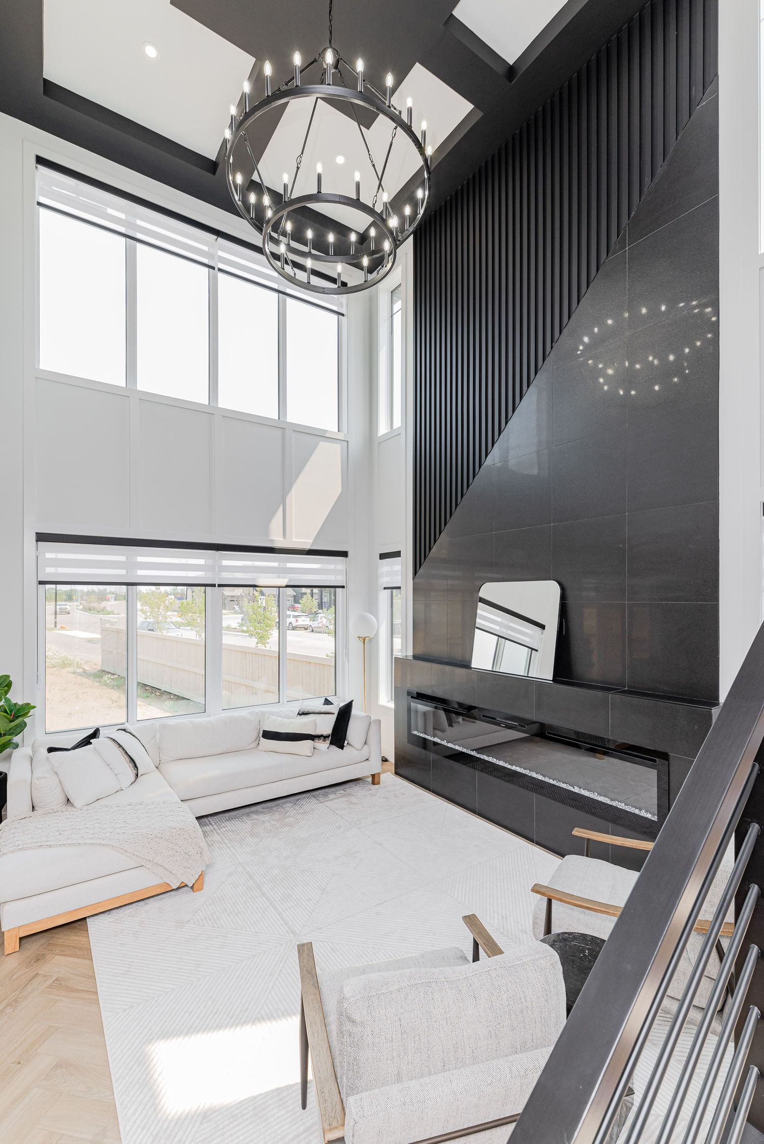 Modern double-height living room with white sofas, black accent wall, fireplace, and contemporary chandelier.