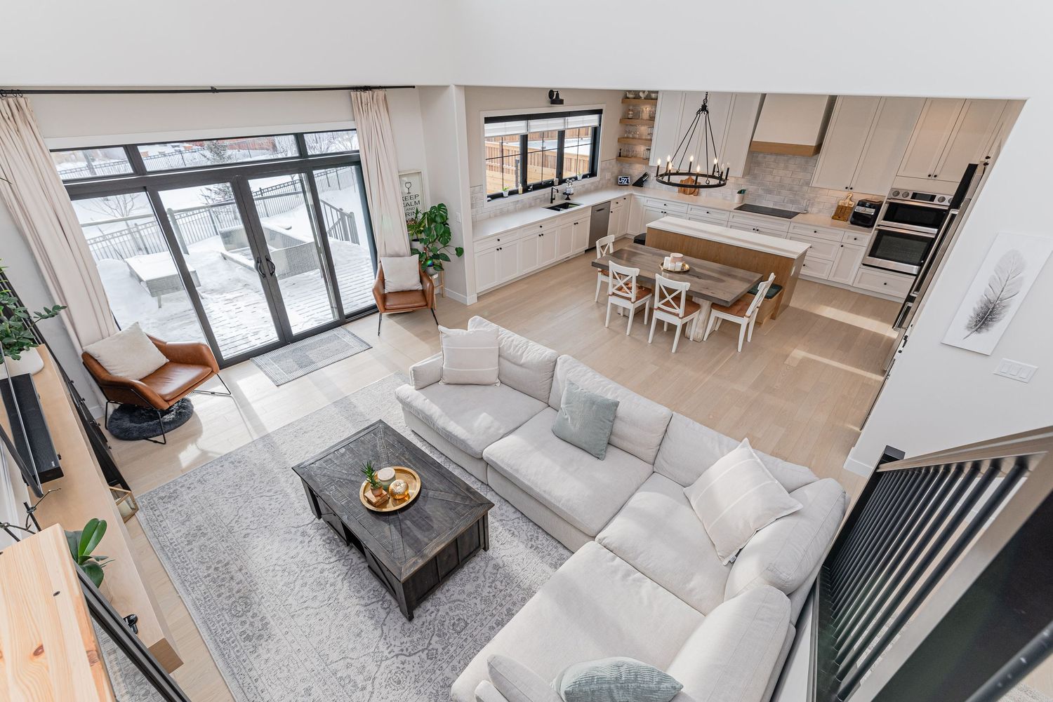 Aerial view of modern open-concept living room with gray sectional sofa, adjoining kitchen, and dining area with natural light.
