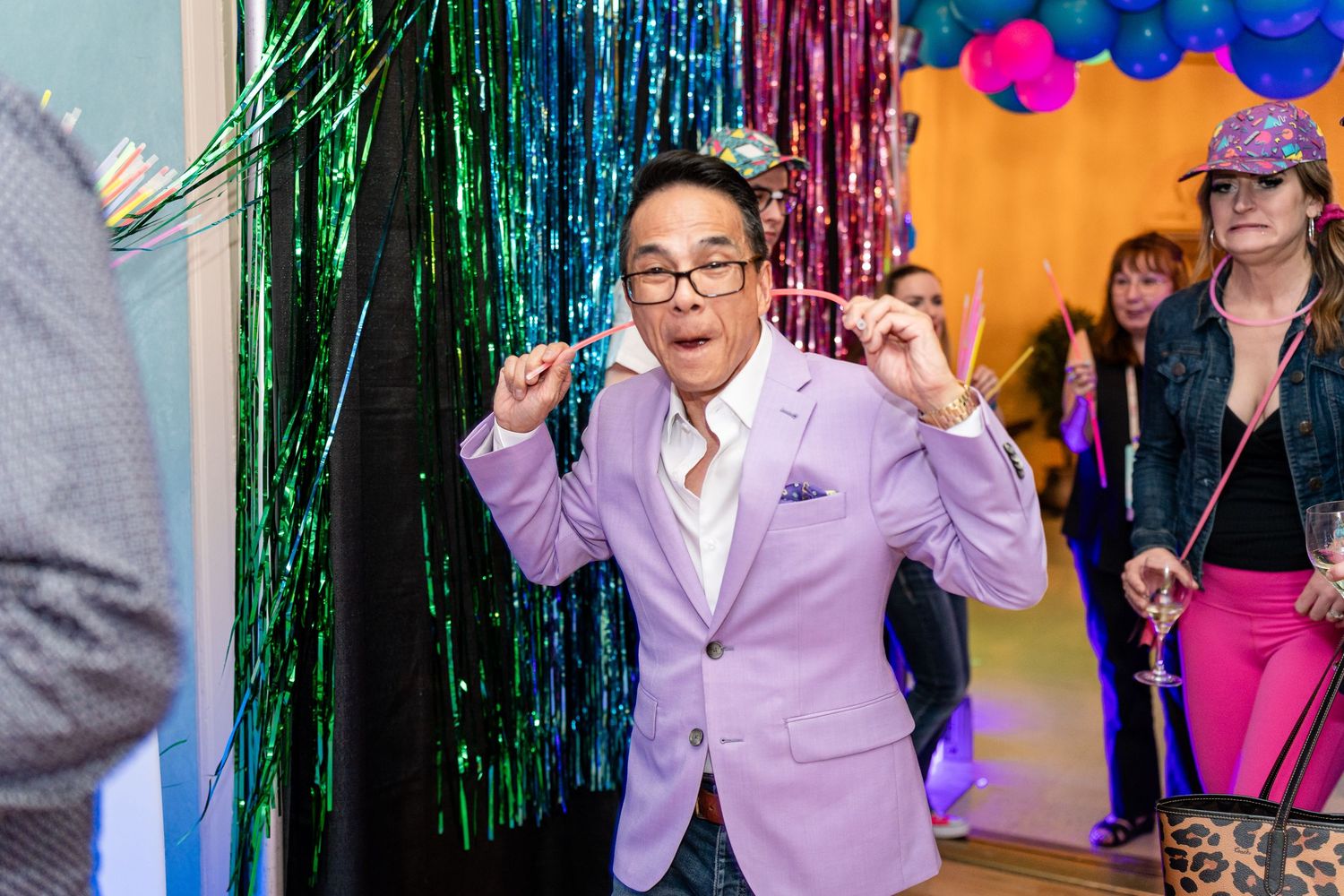Energetic party scene with someone in a lavender blazer dancing against sparkly decorations.