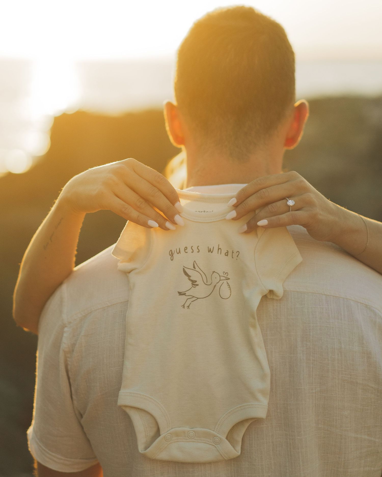 A series of sunset-lit photos showing someone holding up a small white baby onesie against a warm glowing background.