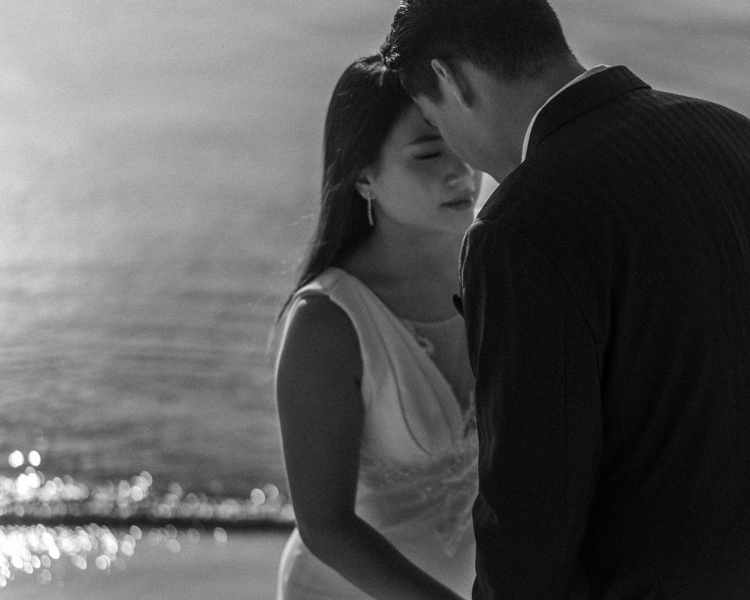 Black and white photo series showing a romantic couple embracing and kissing on a beach at sunset.