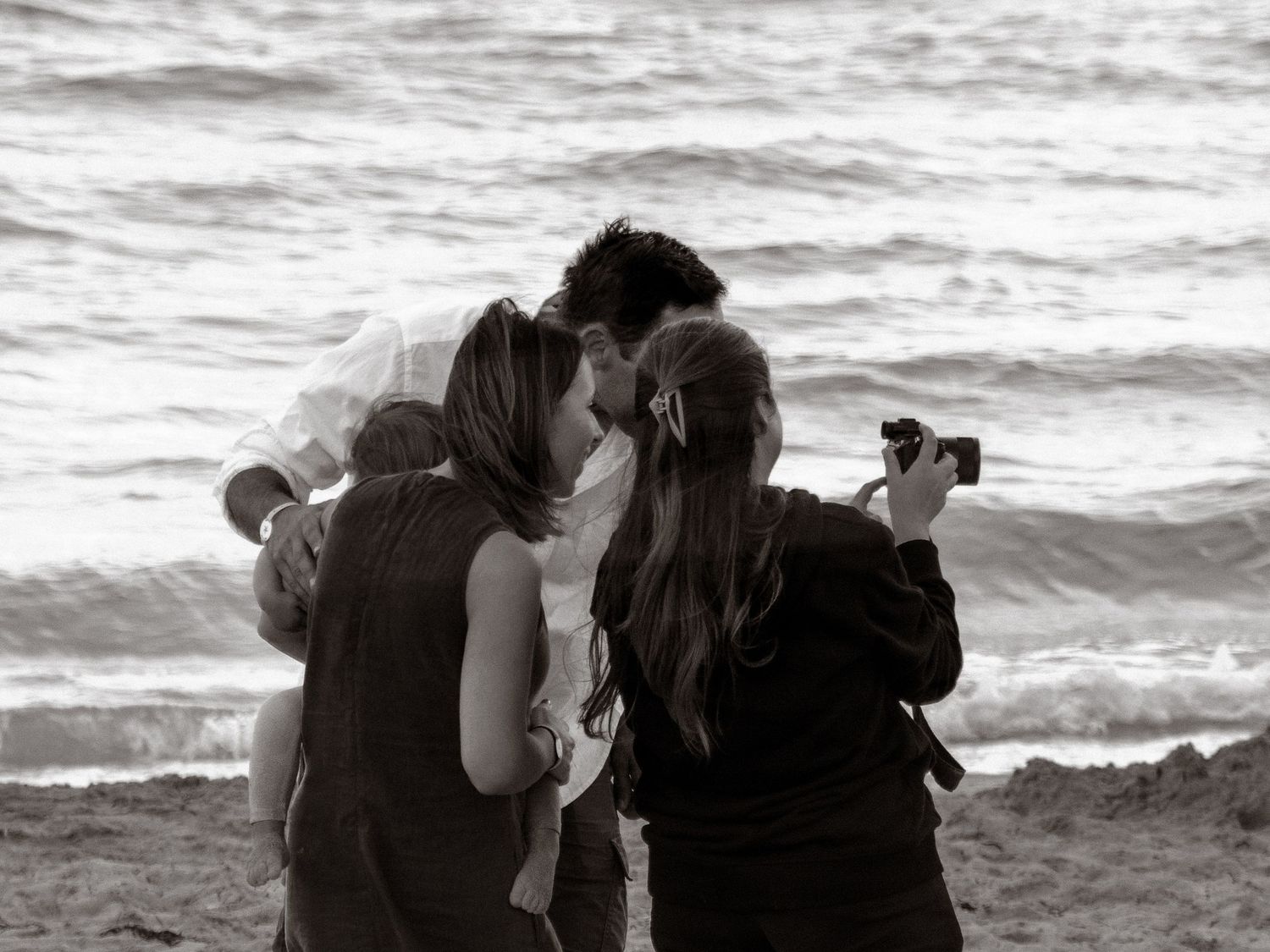 A photographer captures a romantic black and white moment between a couple by the ocean waves.