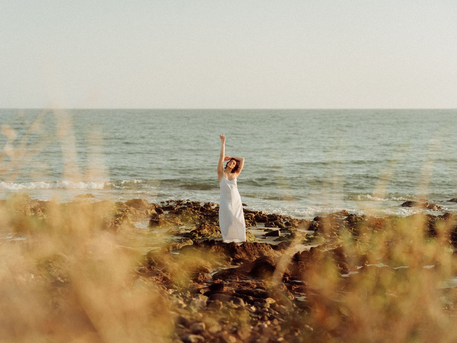 A couple poses on a rocky beach at sunset with ocean waves in the background.