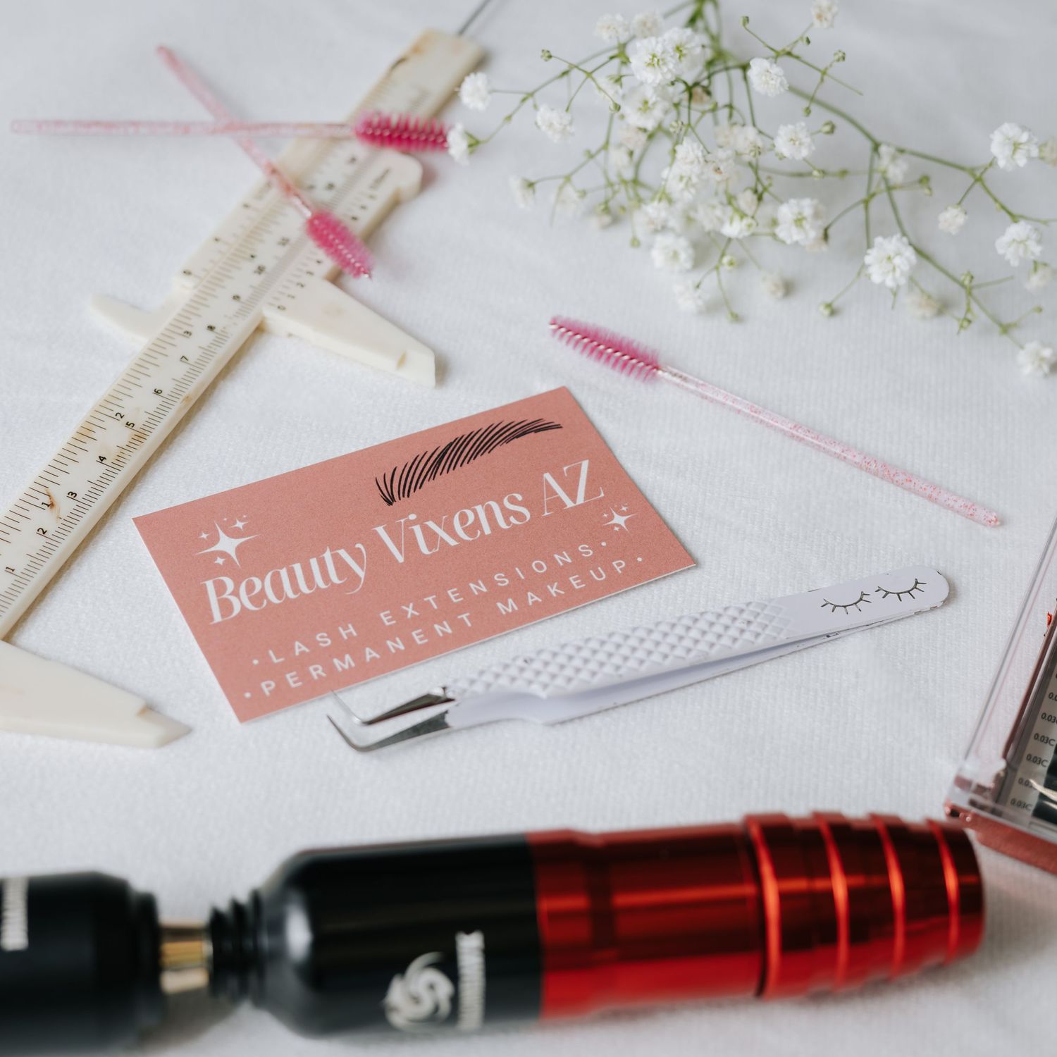 Flatlay of beauty products and tools with delicate white flowers on light background.