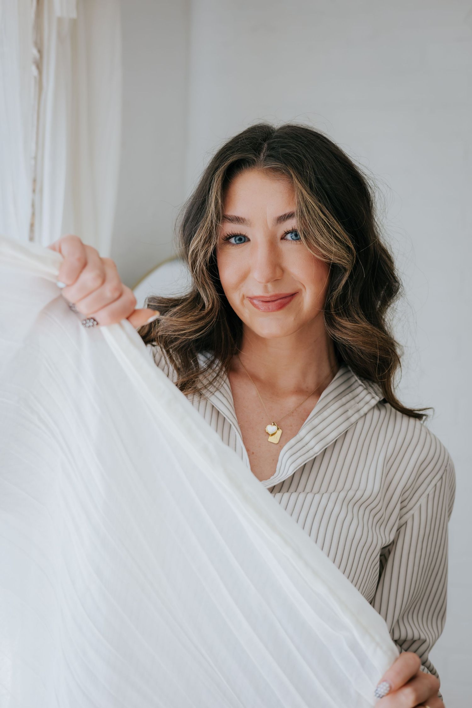 Someone in a beige sweater playfully holding up white fabric against a light background.