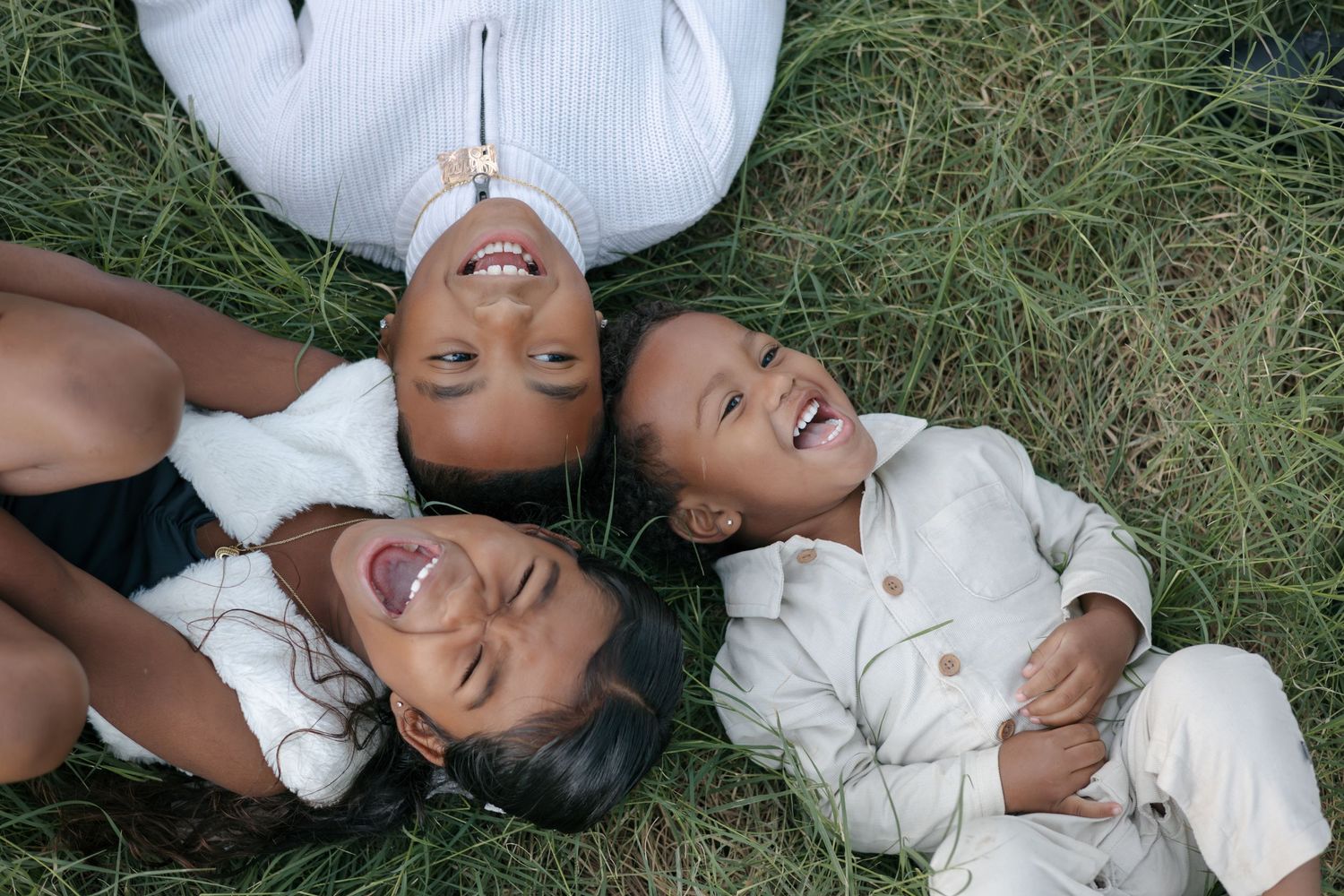 Family lying in grass sharing genuine laughter during outdoor photo session.