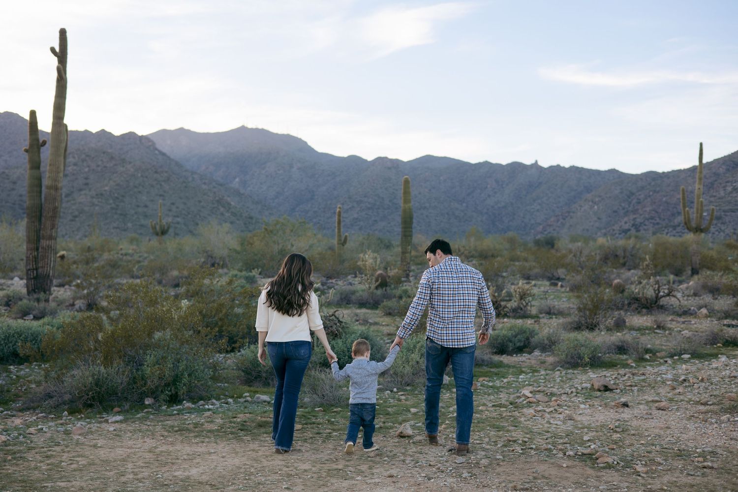 Family walking together in desert landscape with saguaro cacti.
