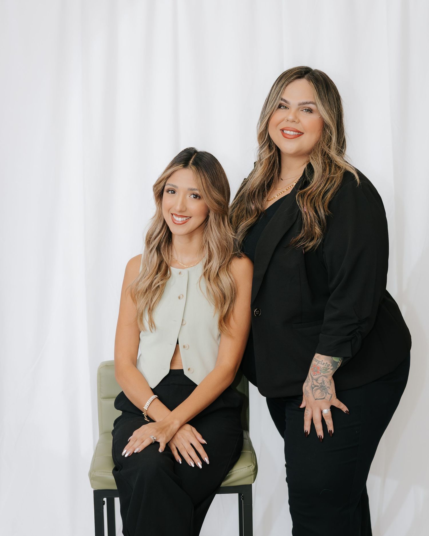 Two women in black and white outfits laughing and posing together in a photo studio against white backdrop.