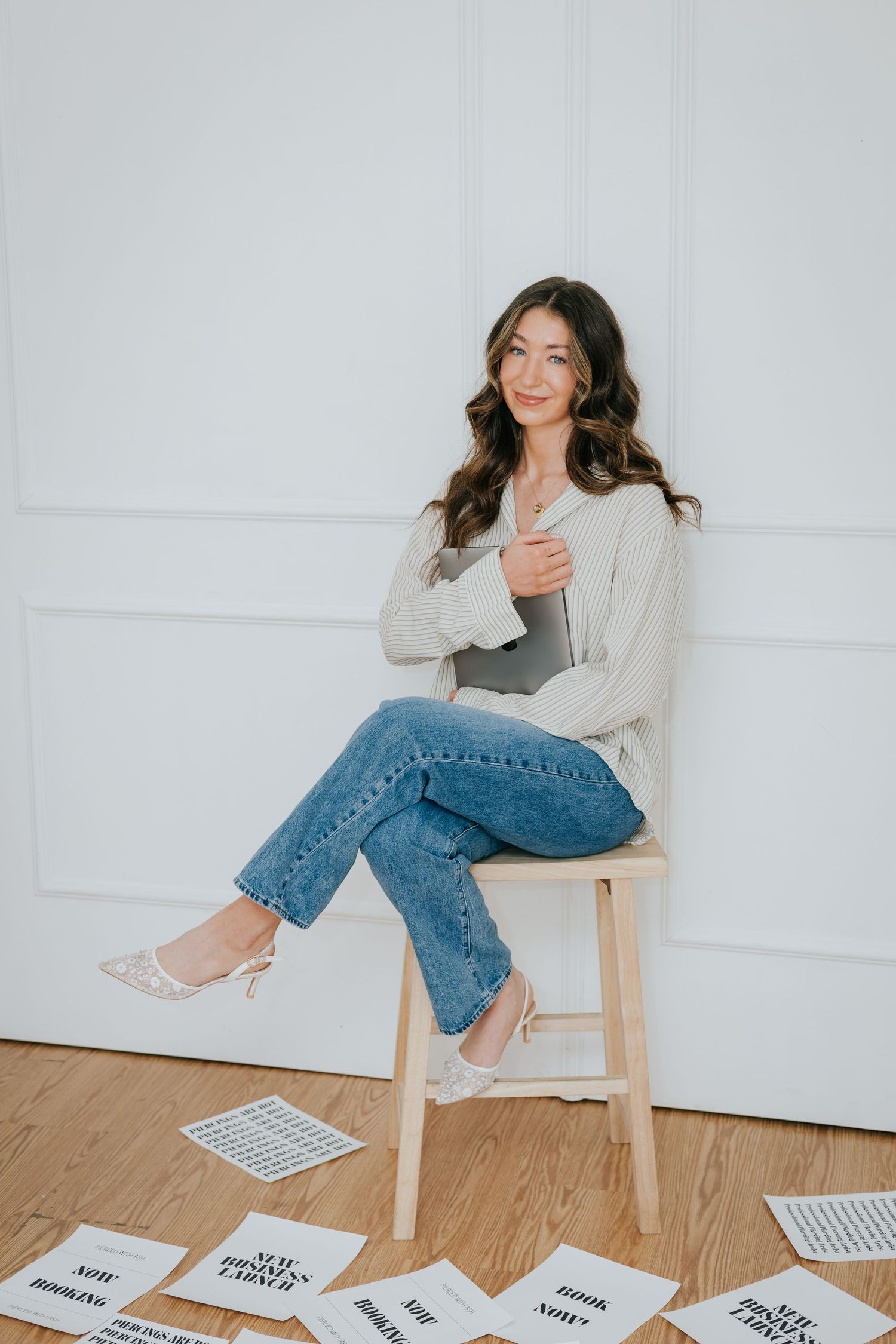 Person in casual attire sitting on wooden chair with papers spread on floor.