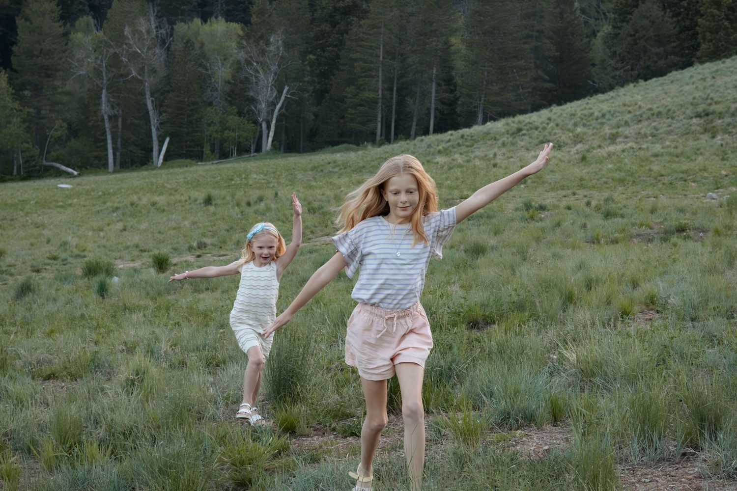 People joyfully running through a grassy mountain meadow during golden hour.