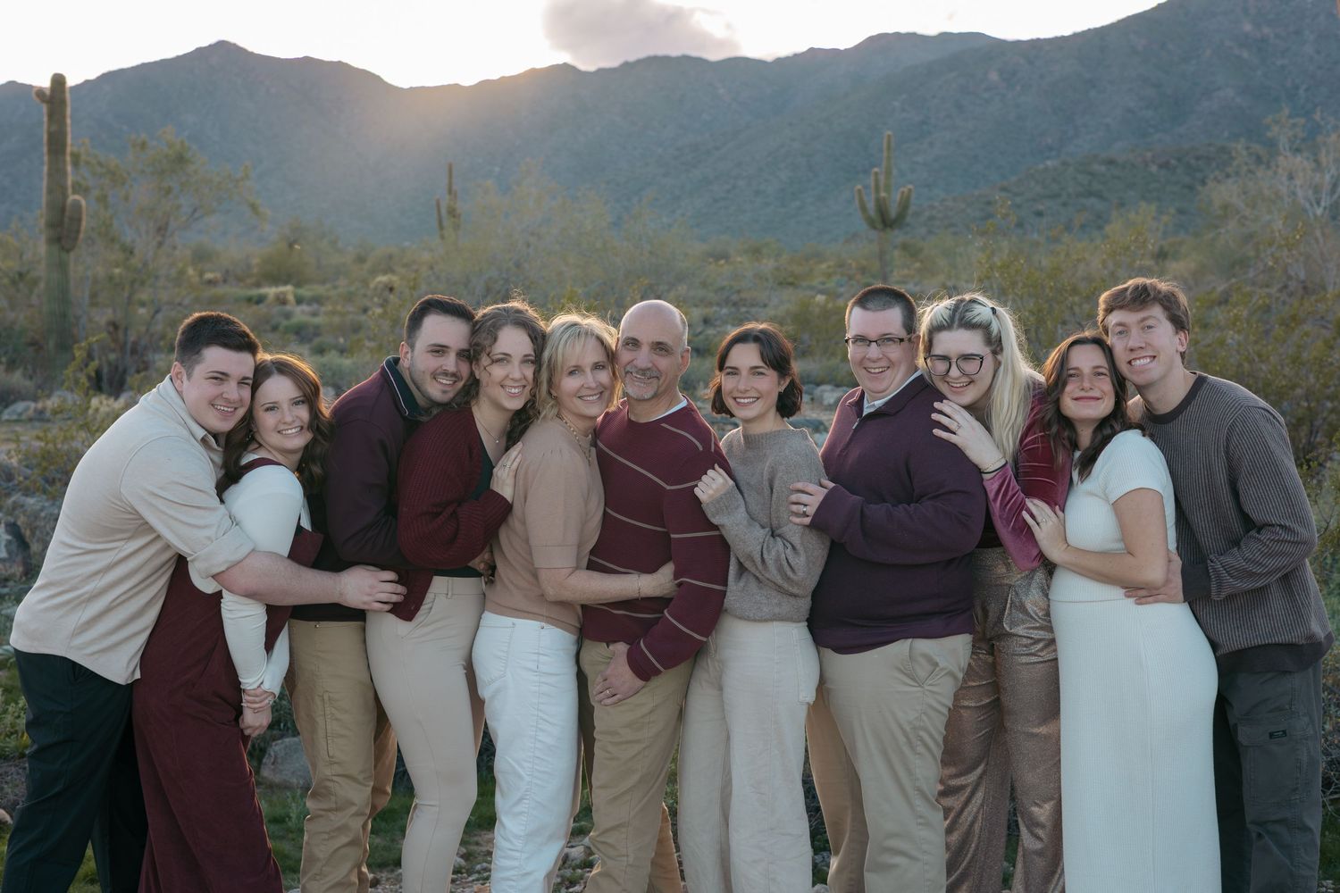 Group photo of friends hugging together at sunset with mountain backdrop.