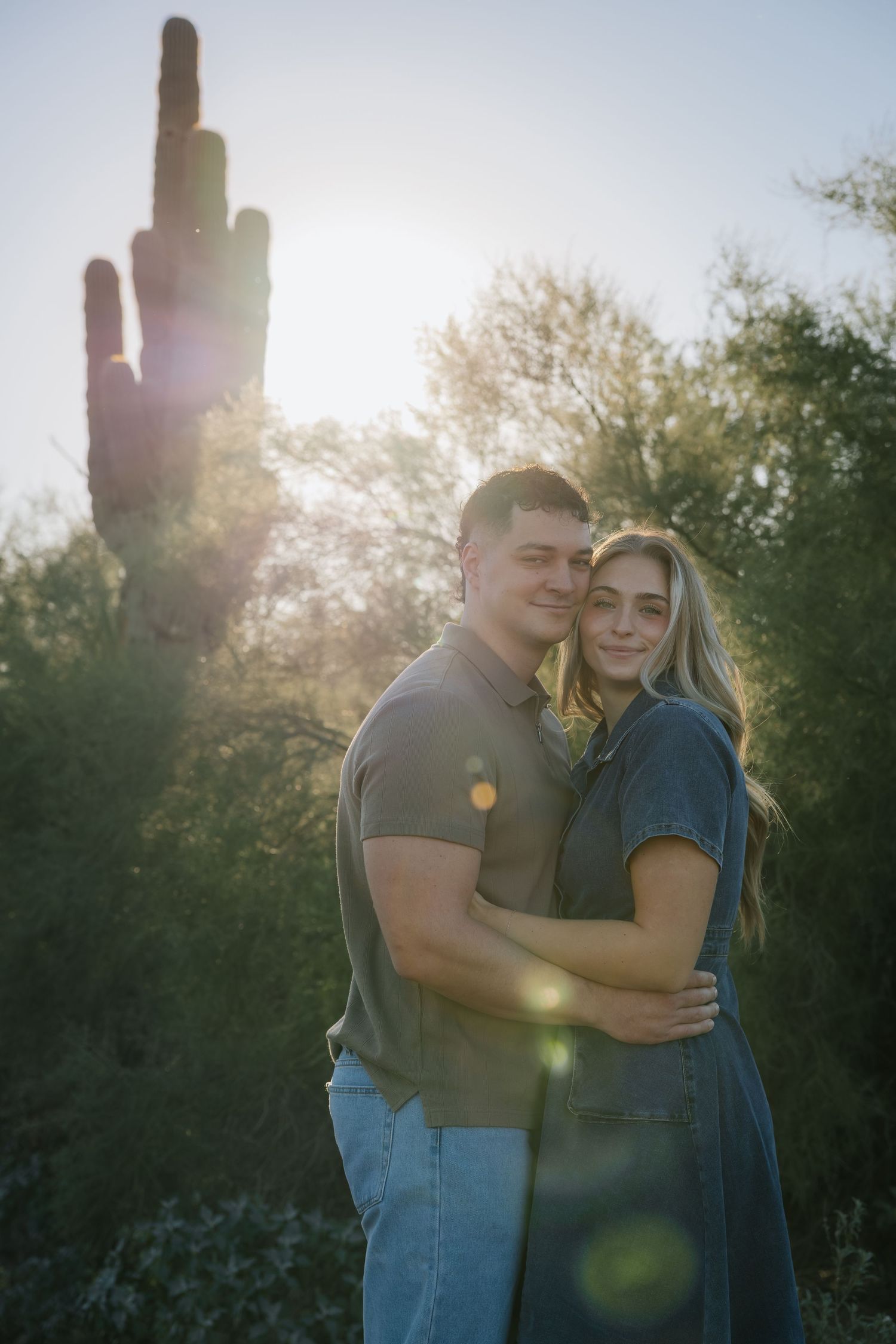 Couple embracing in desert landscape with saguaro cactus and sunset backlight.