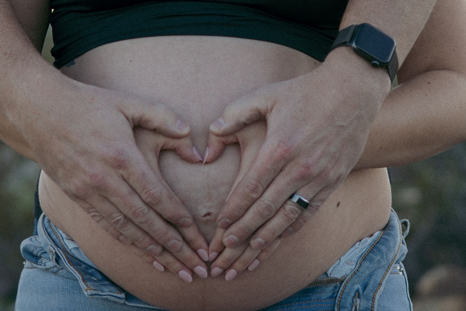 Hands forming heart shape over pregnant belly in denim.