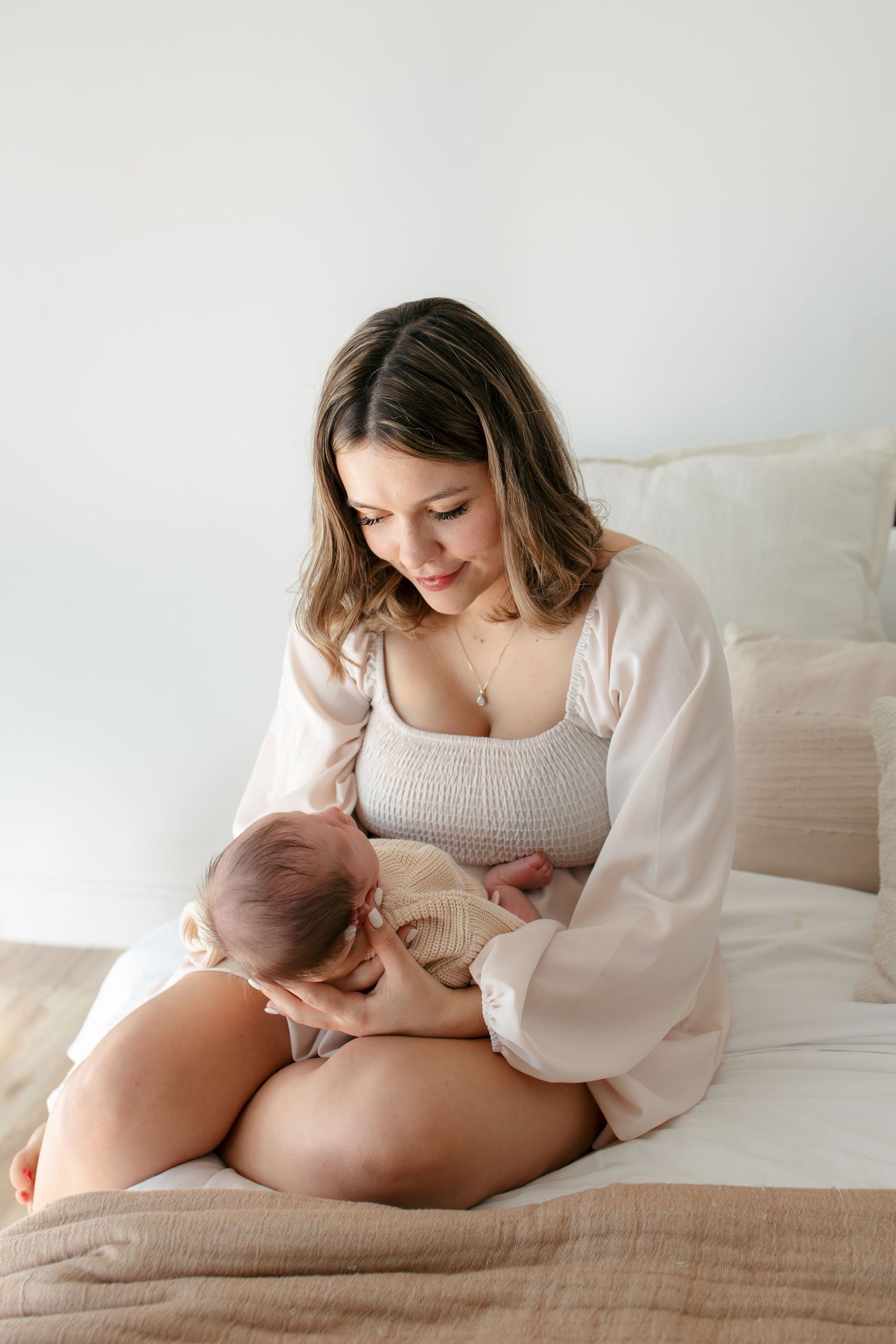 Mother in white robe nurturing baby on bed with soft lighting.