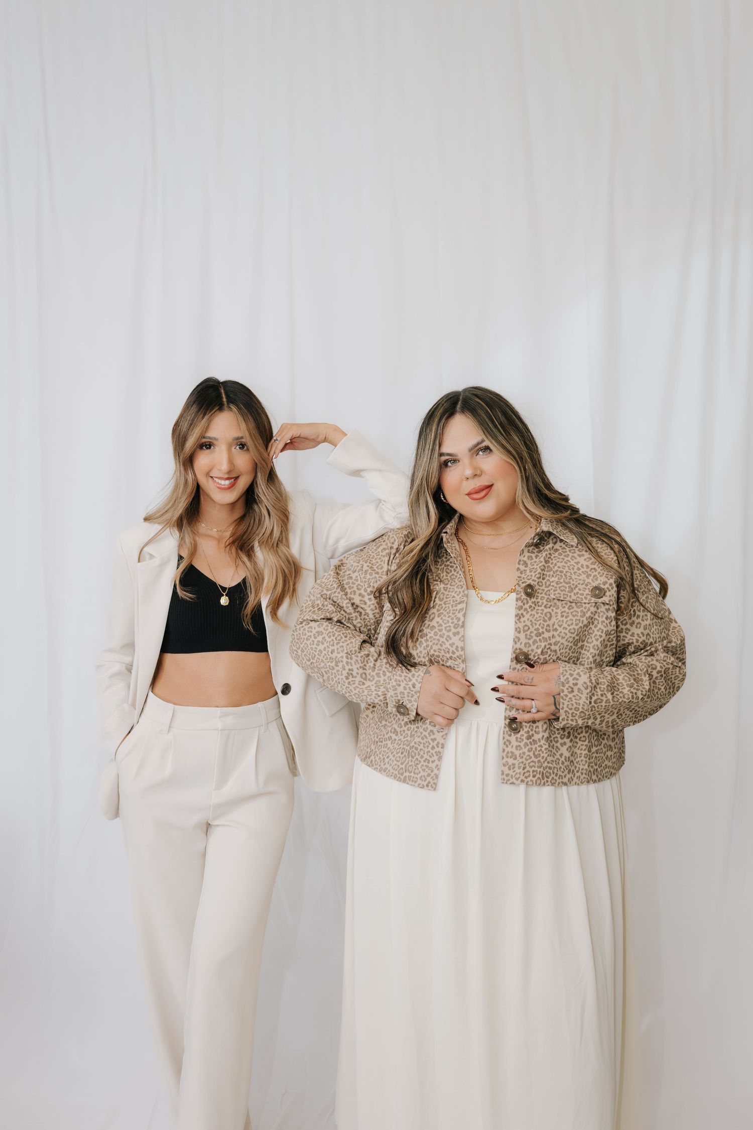 Two friends in neutral tones posing together for lifestyle photoshoot against white background.