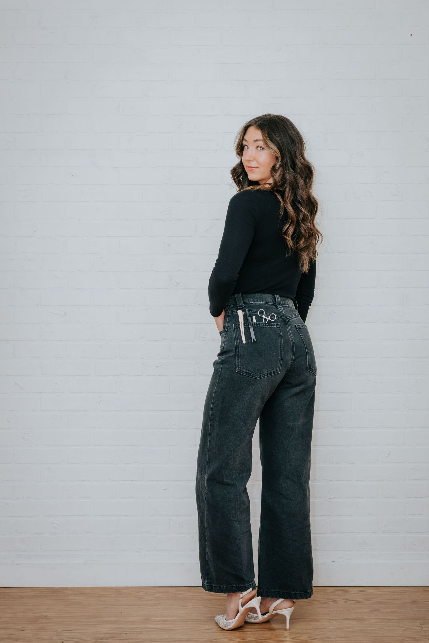 Person wearing black top and wide-leg jeans poses against light gray wall.