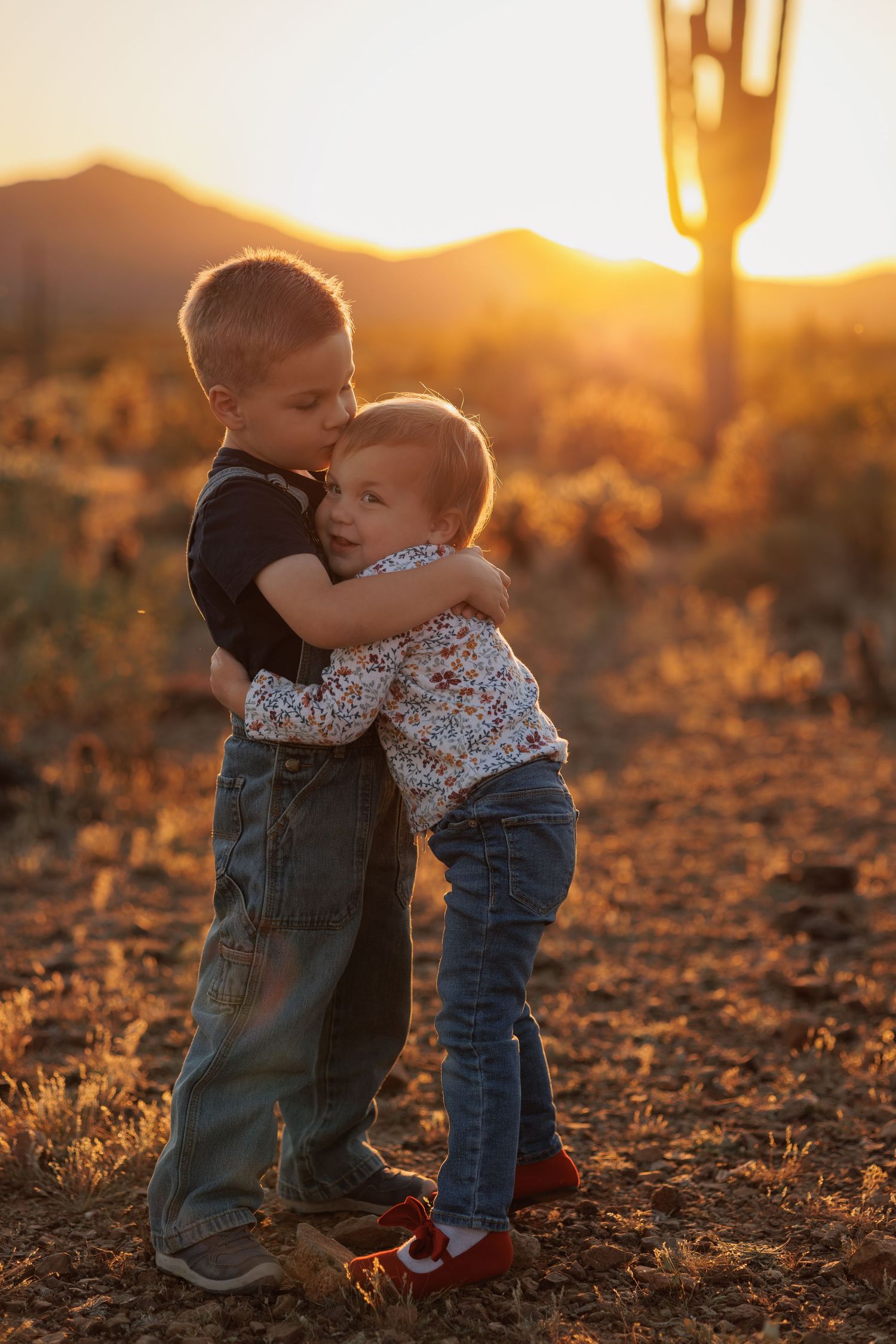 Two children hugging in desert setting during golden hour.