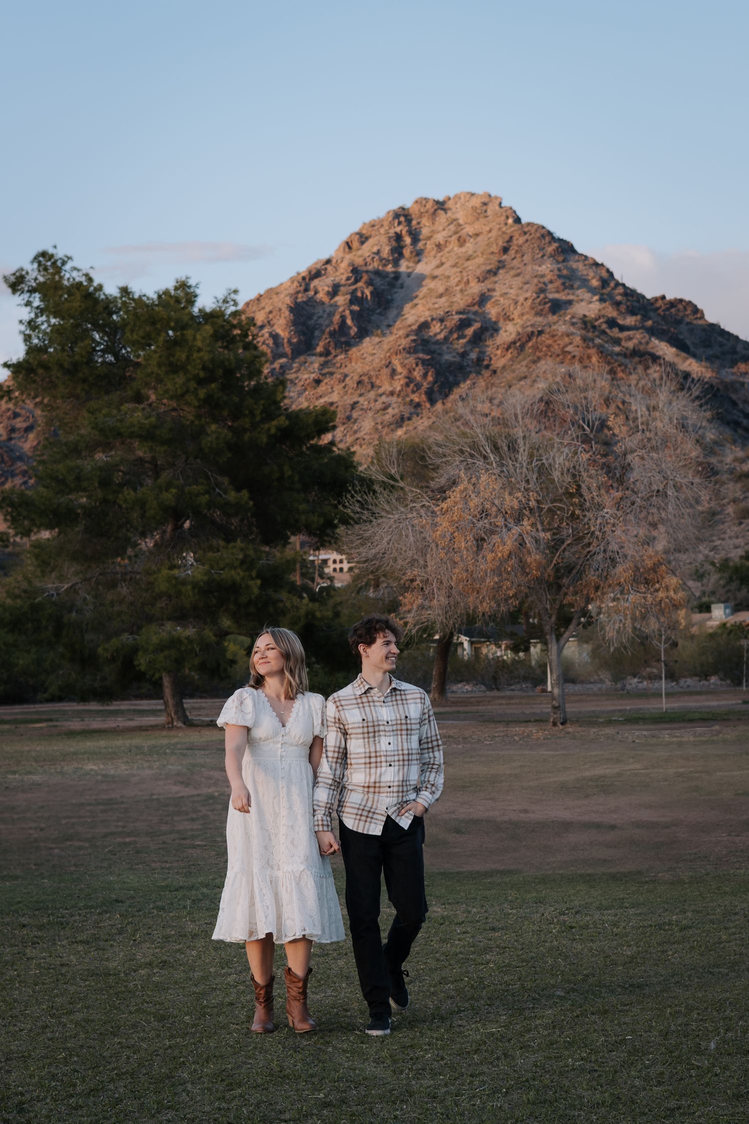 Couple walking through a park with mountain peaks glowing in sunset light.
