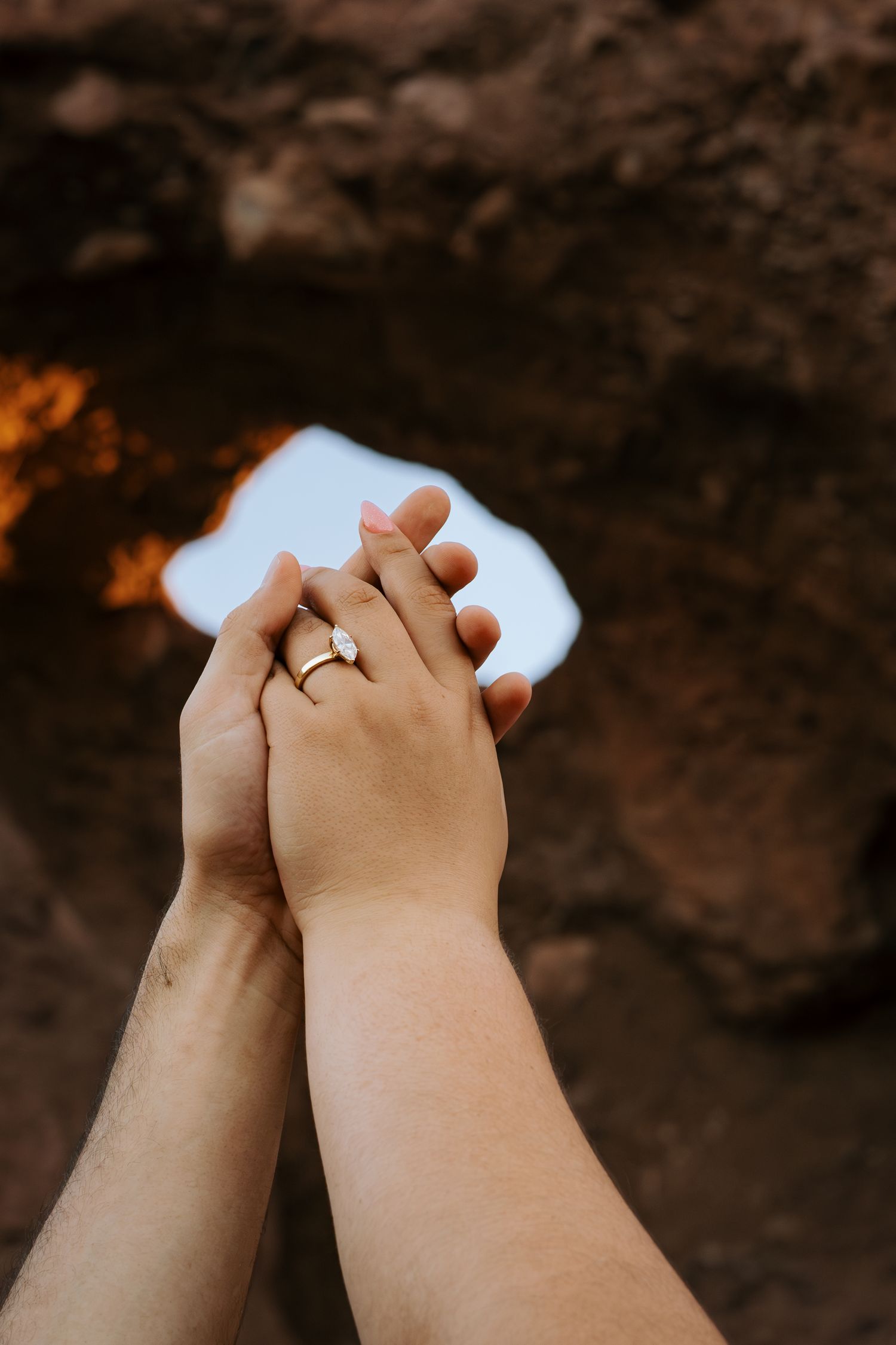 Close-up of two hands clasped together showing wedding rings against a dark background.