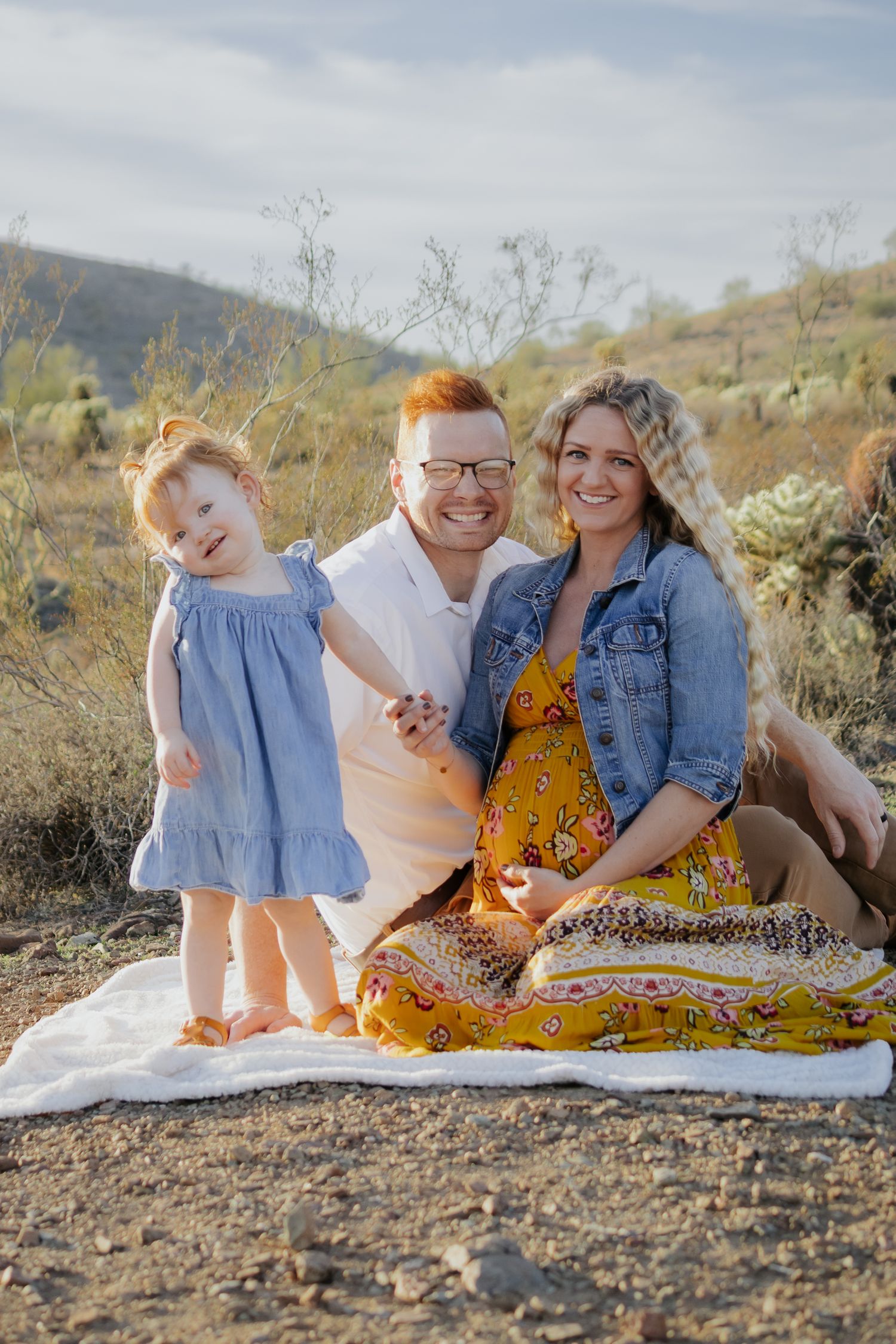 A family sits on a blanket for a casual outdoor photoshoot in desert terrain.