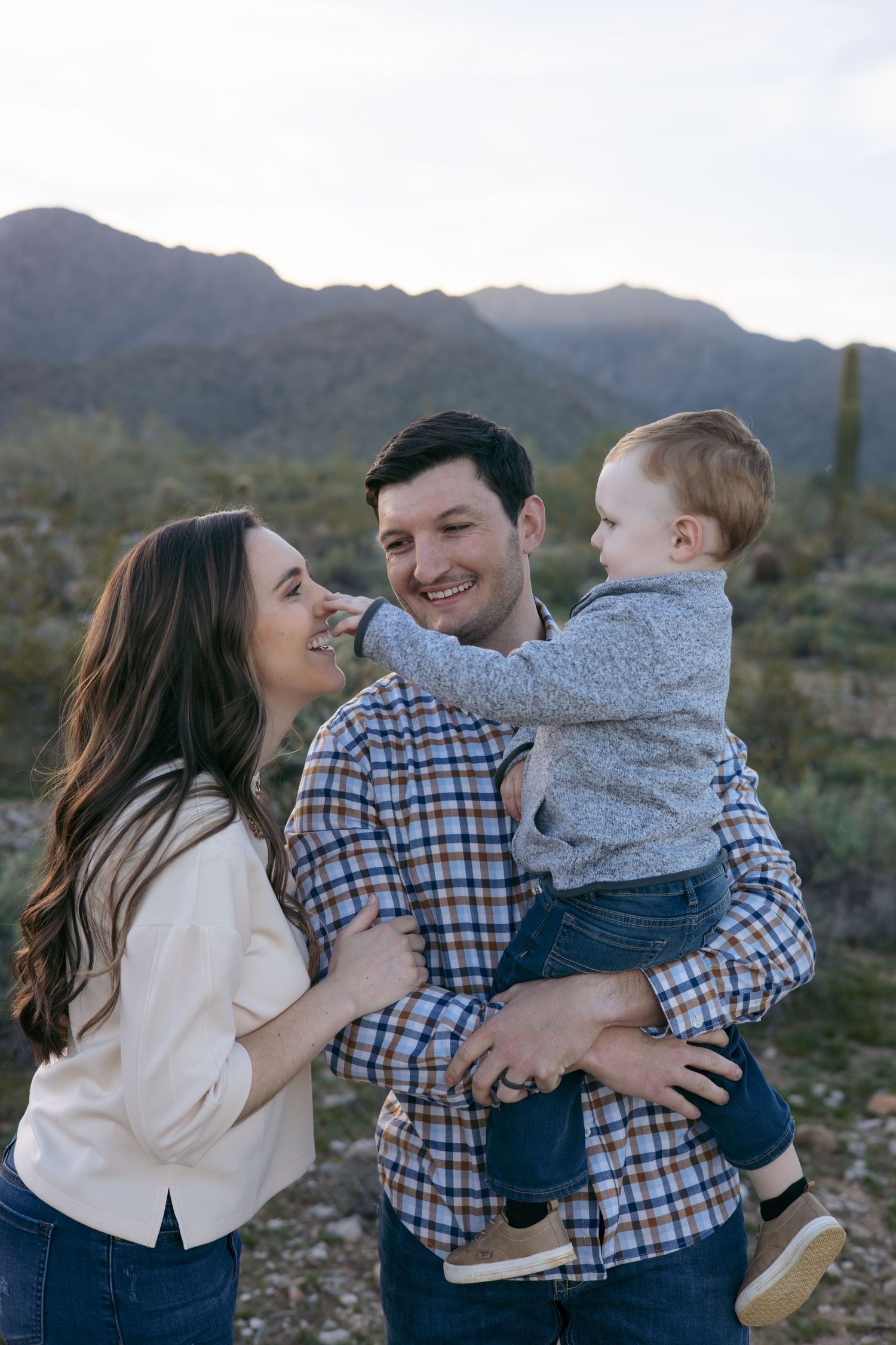 Family portrait in desert landscape with mountains and cacti at golden hour.