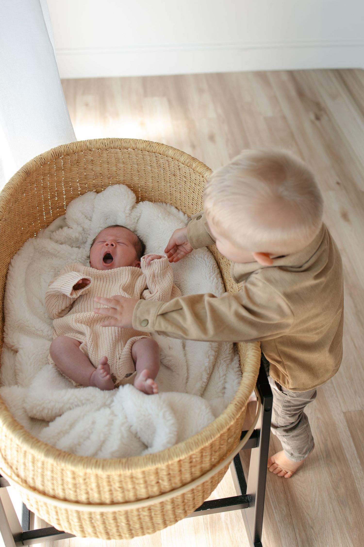 Baby lying in a round wicker bassinet while being gently touched.