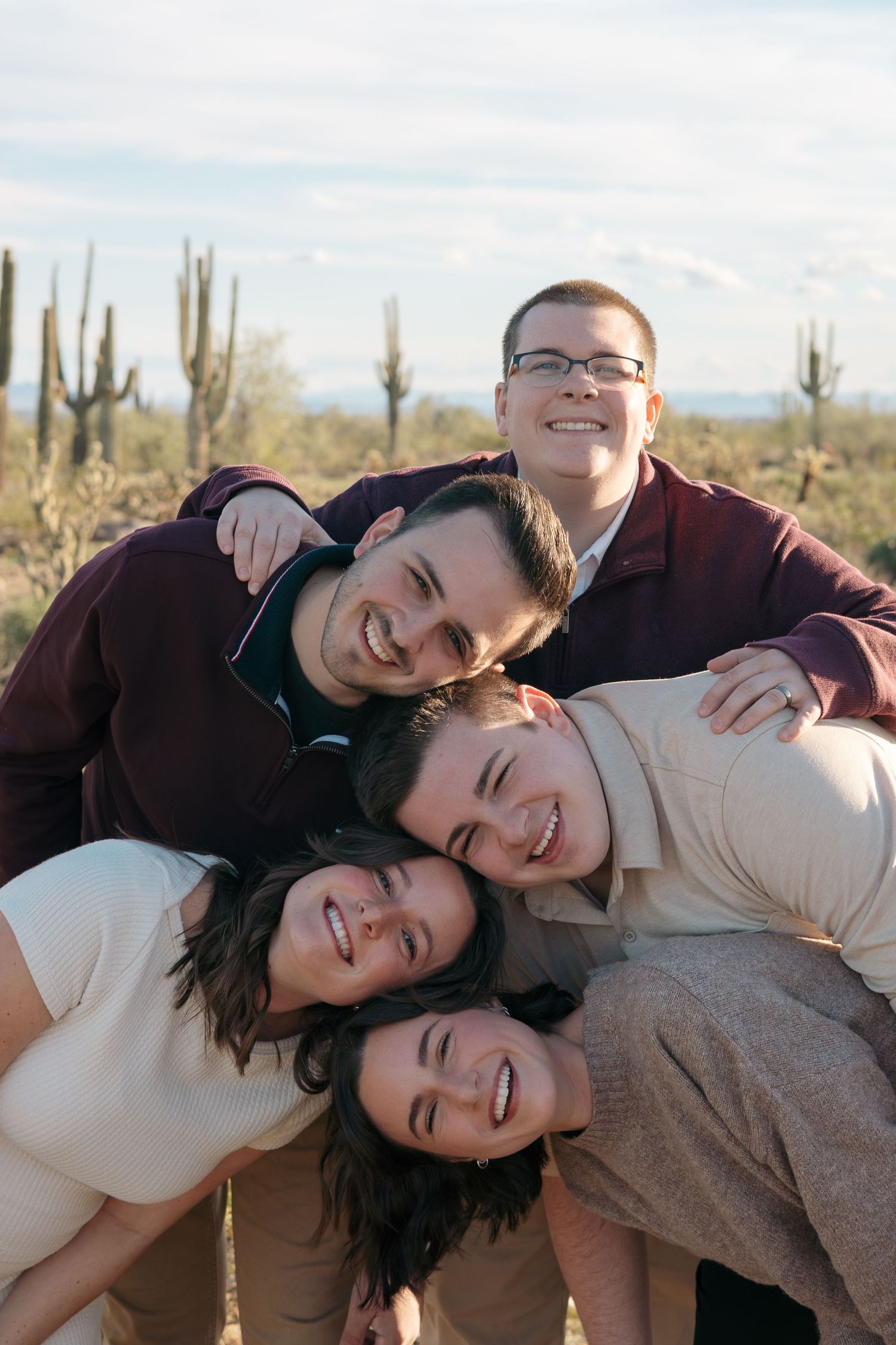 Friends laughing together in playful stack pose with desert landscape background.