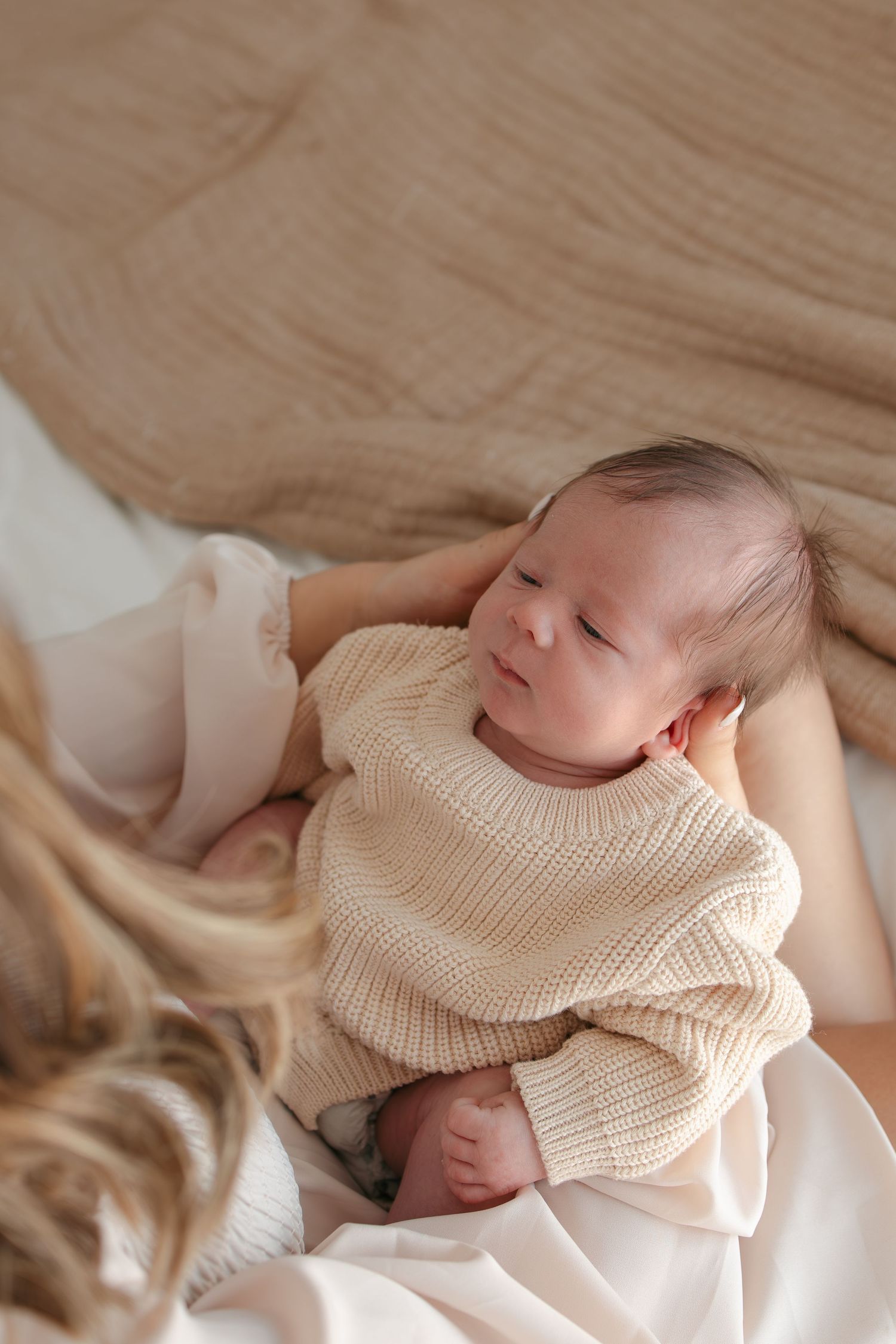 Sleeping newborn in cream knit sweater on soft beige bedding.