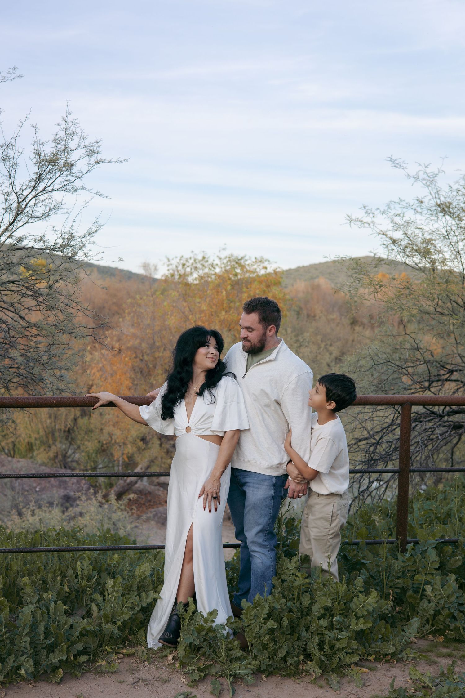 Family in white outfits posing on rustic railing with desert mountains in background.