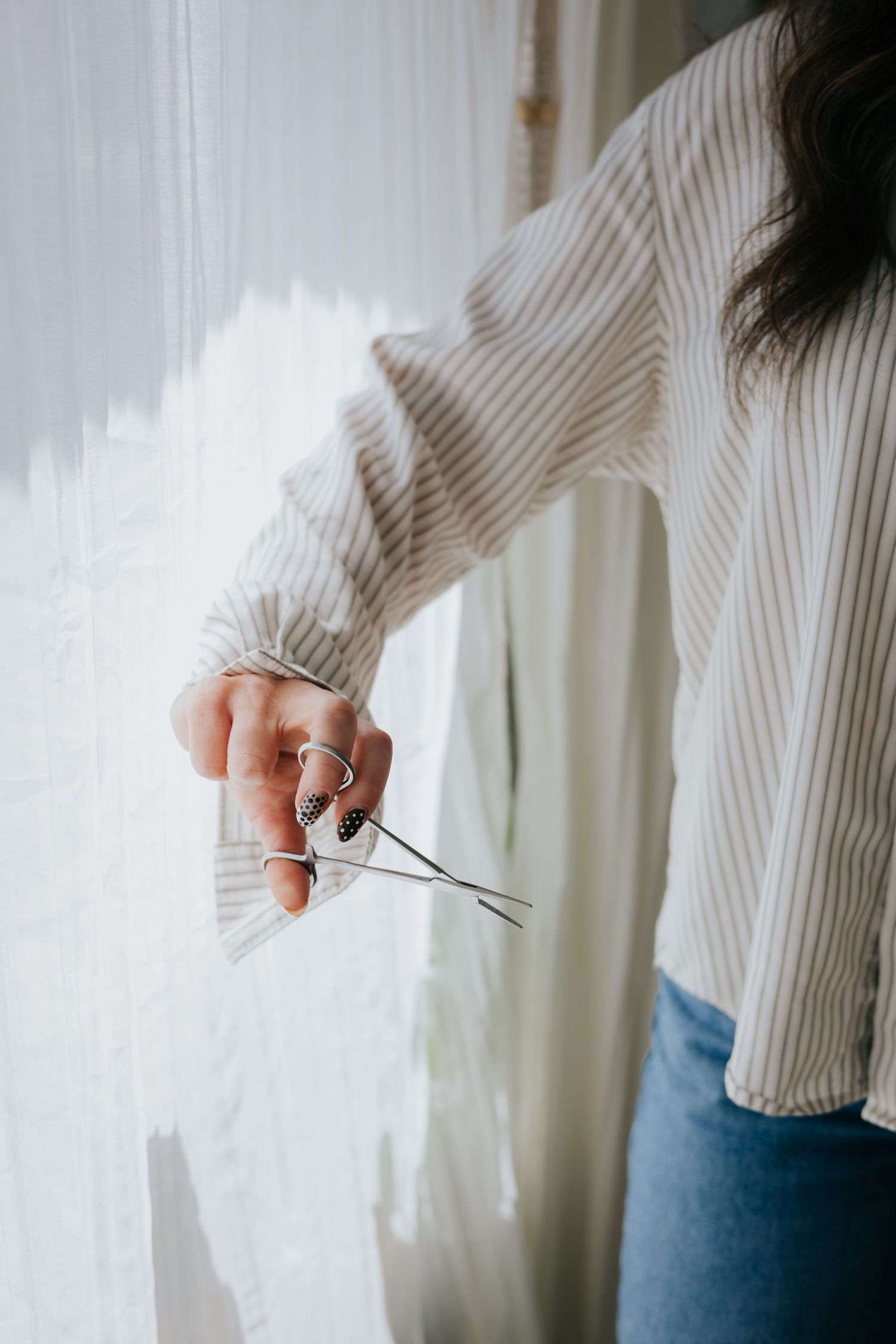Close-up of hands holding scissors near white curtains in natural light.