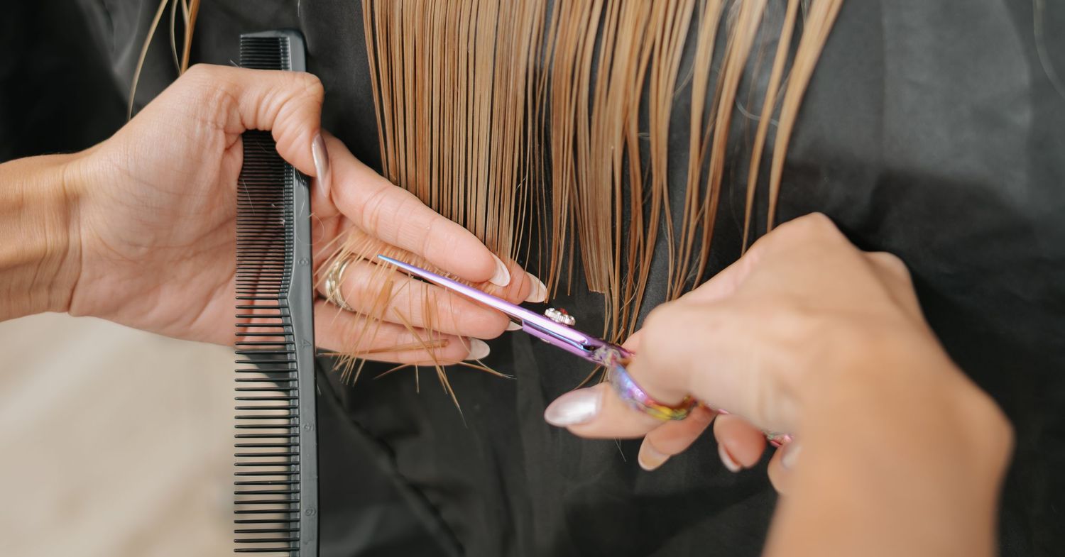 Professional hairstylist sectioning and cutting hair with scissors in salon.