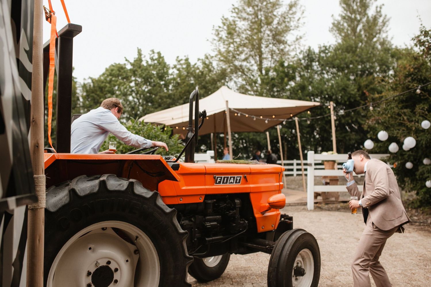 Orange vintage tractor parked under white tent canopy at outdoor event.