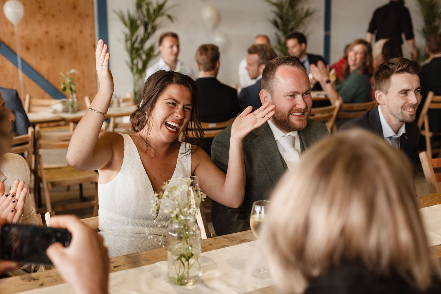 Wedding reception guests celebrate with enthusiasm in a warmly lit indoor venue.