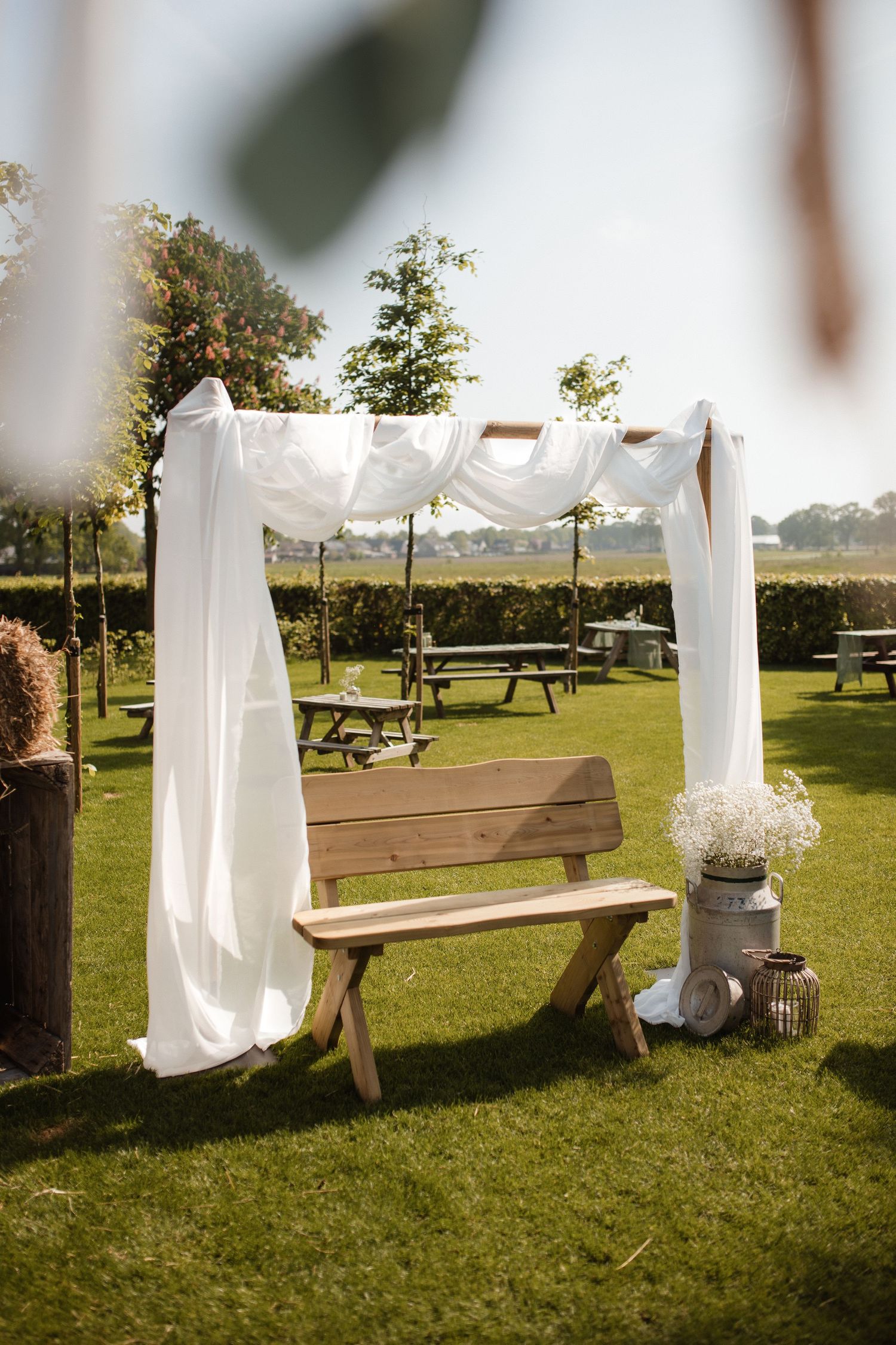 White draped fabric and wooden benches create an elegant outdoor wedding ceremony setup on a grassy lawn.