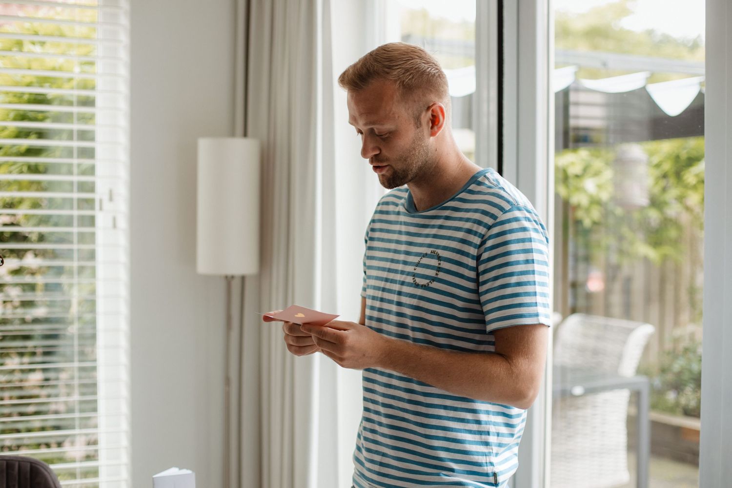 Person in striped shirt standing by window in bright modern interior.