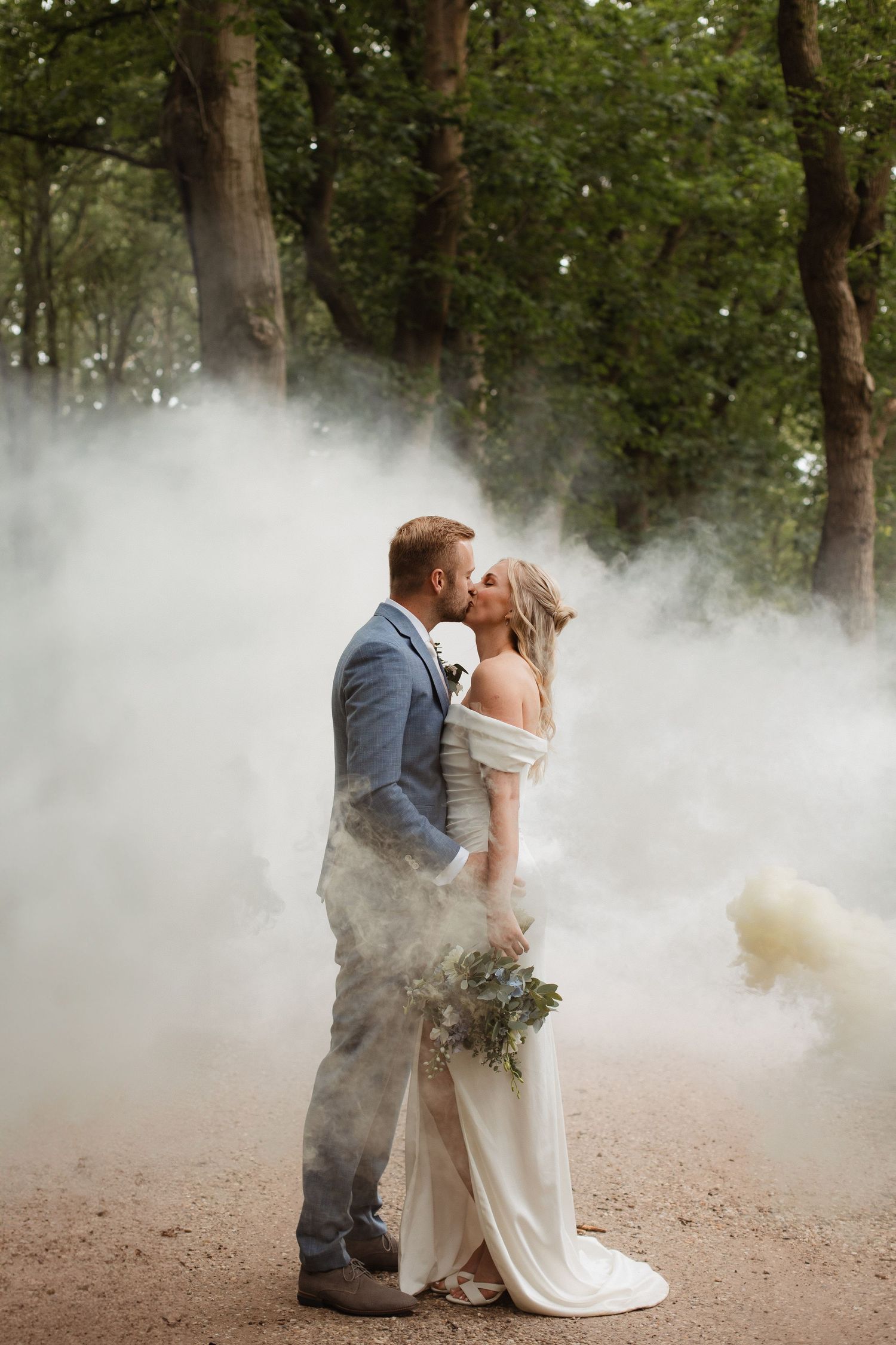 A dreamy wedding photo with smoke effects surrounding a couple in a wooded setting.