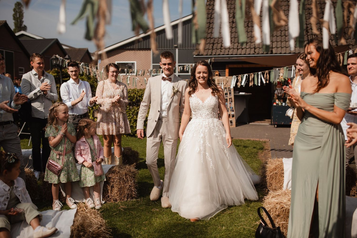 Wedding guests in light-colored attire gather outdoors for a celebration.