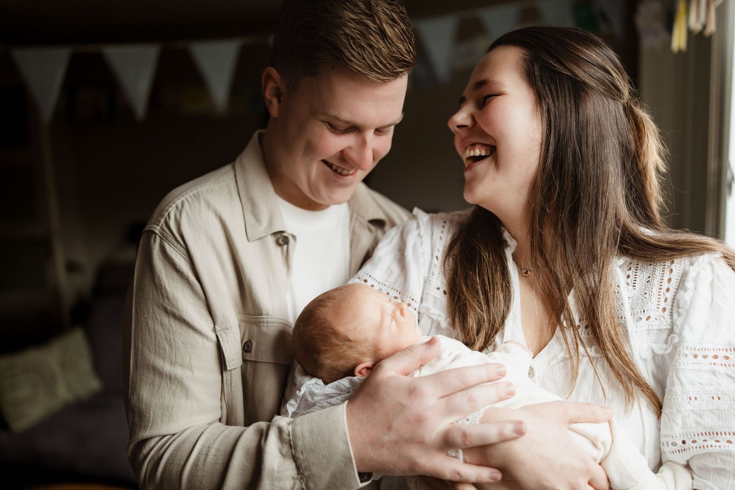 Ouders lachen samen met hun baby tijdens een newbornshoot thuis