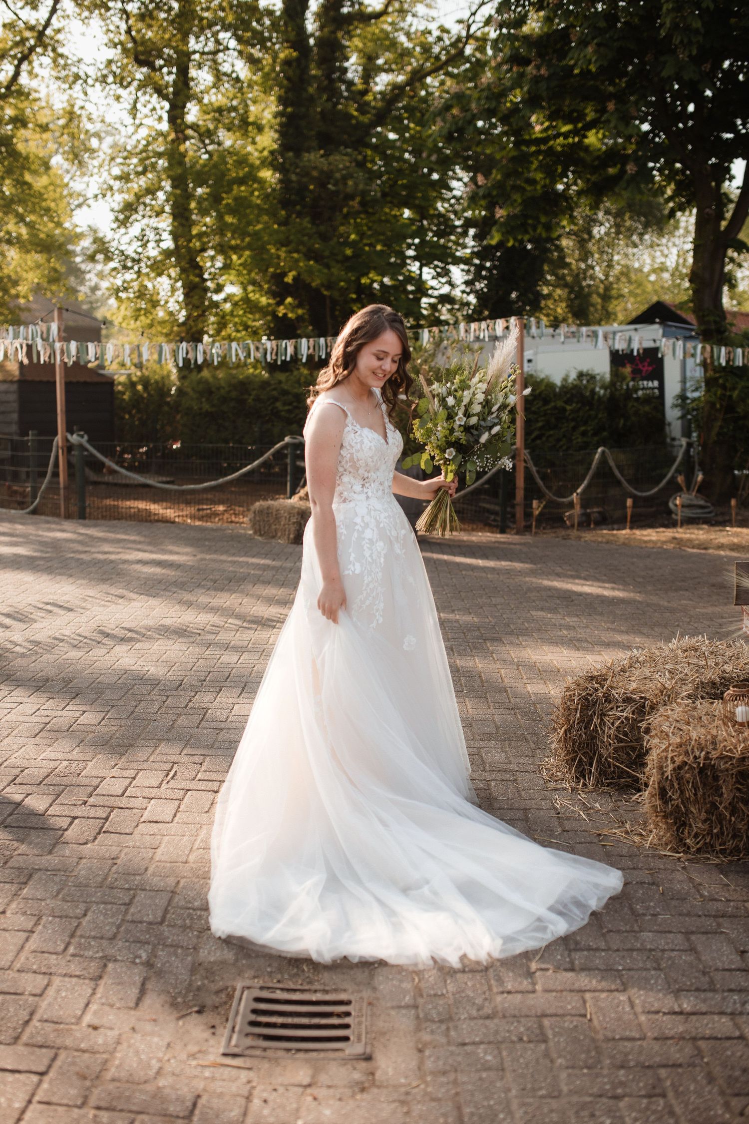 A bride in a flowing white lace gown twirls on a stone patio during golden hour.