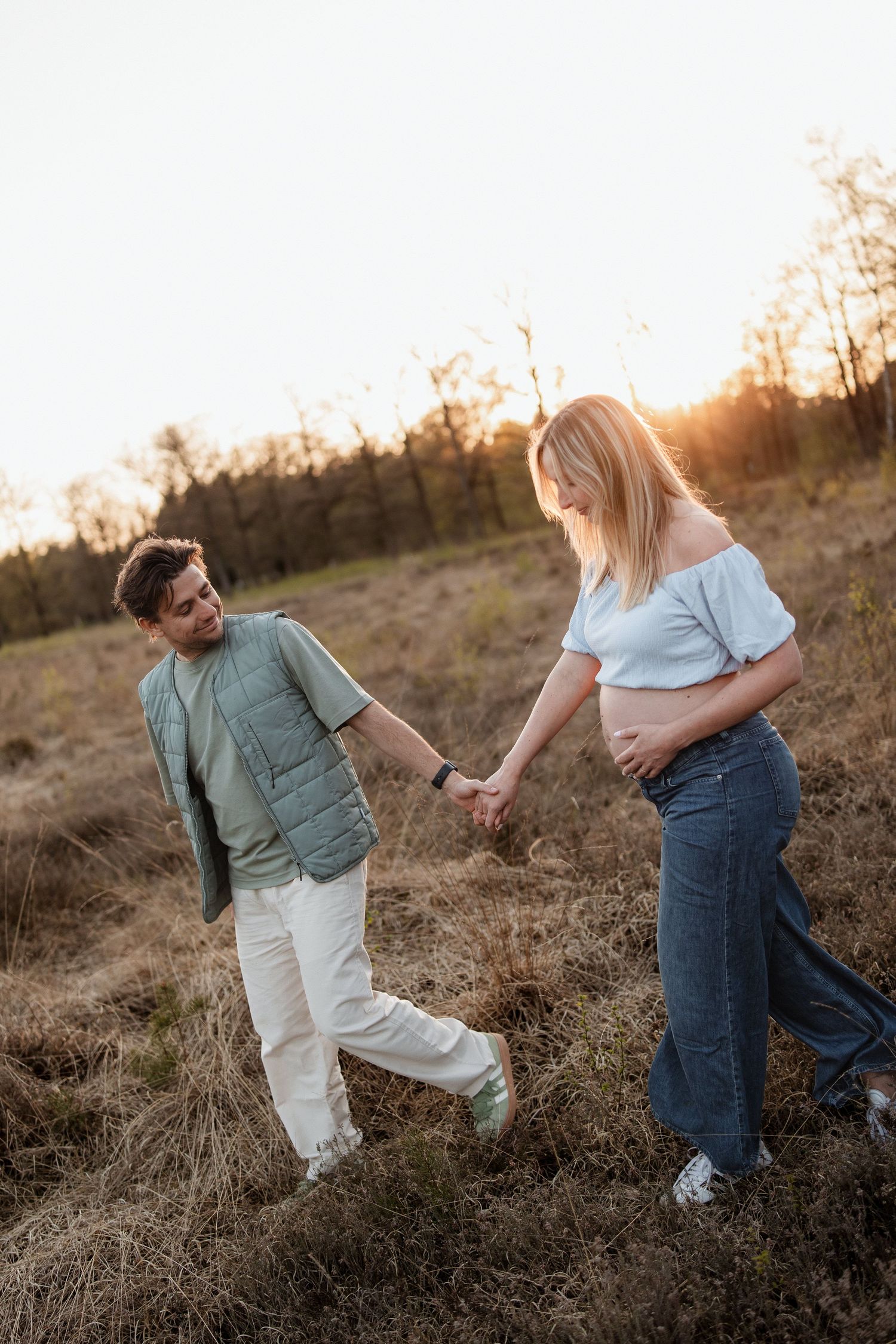 Koppel dat over de hei heen loopt tijdens golden hour en de vrouw is zwanger