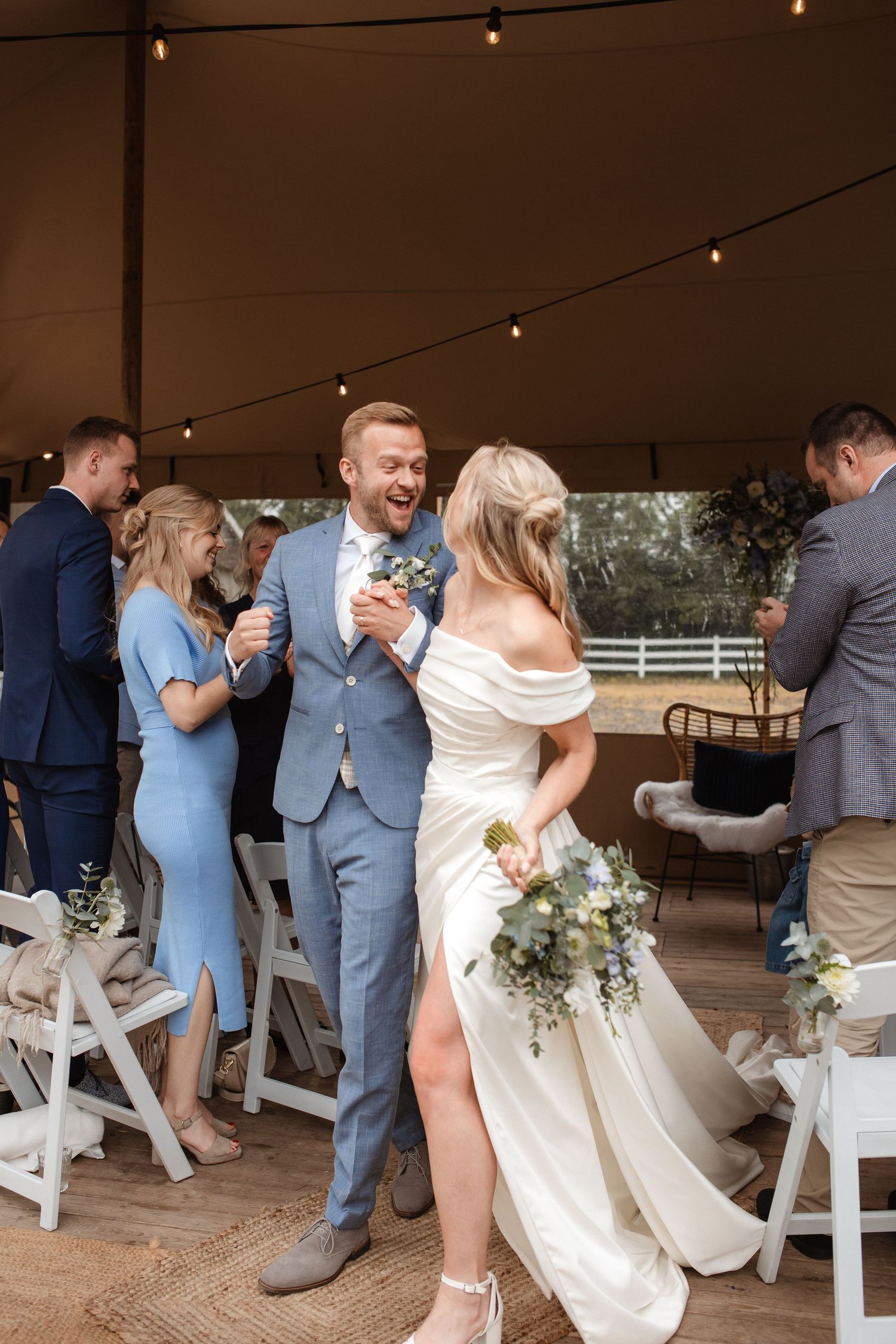 Wedding celebration features multiple couples dancing under string lights in a rustic outdoor venue.